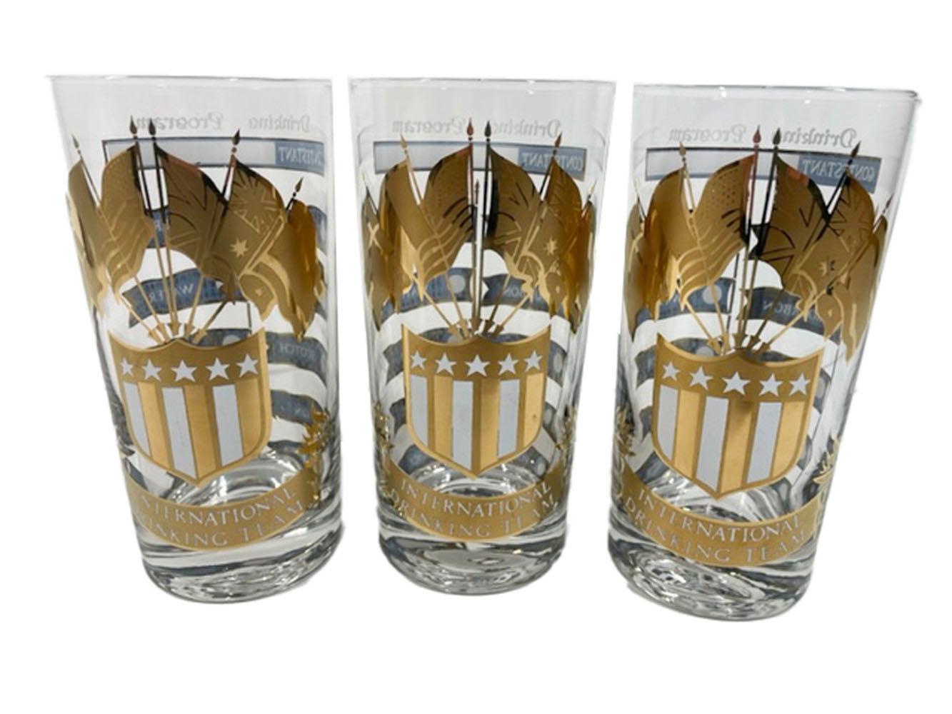 Rare, highball glasses by Culver, LTD. decorated in 22 karat gold with blue and white enamel, in the 'International Drinking Team' pattern. Each decorated on the front with a shield holding five flags above a banner with the words 'International
