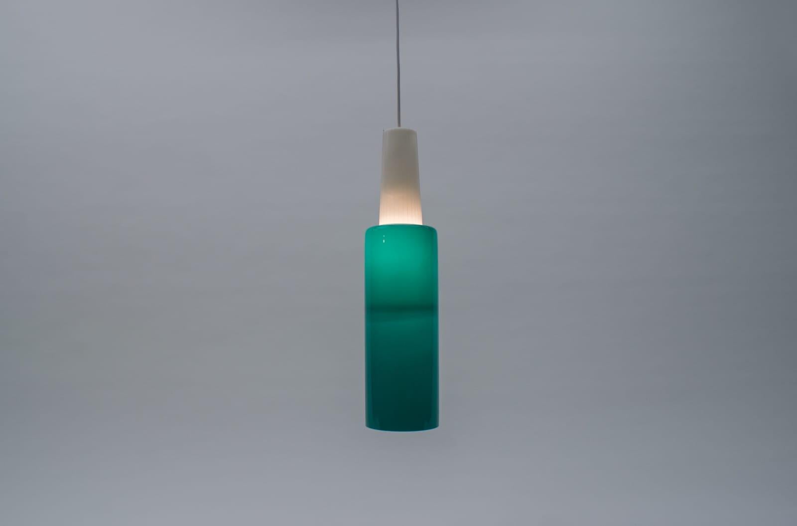 Rara lampada cilindrica in vetro color petrolio.

La parte bianca è realizzata in plastica scanalata, mentre il cilindro color petrolio è in vetro.

Misure: Lunghezza totale con il cavo 135 cm, la lampada stessa 48 cm.

La lampada necessita di
