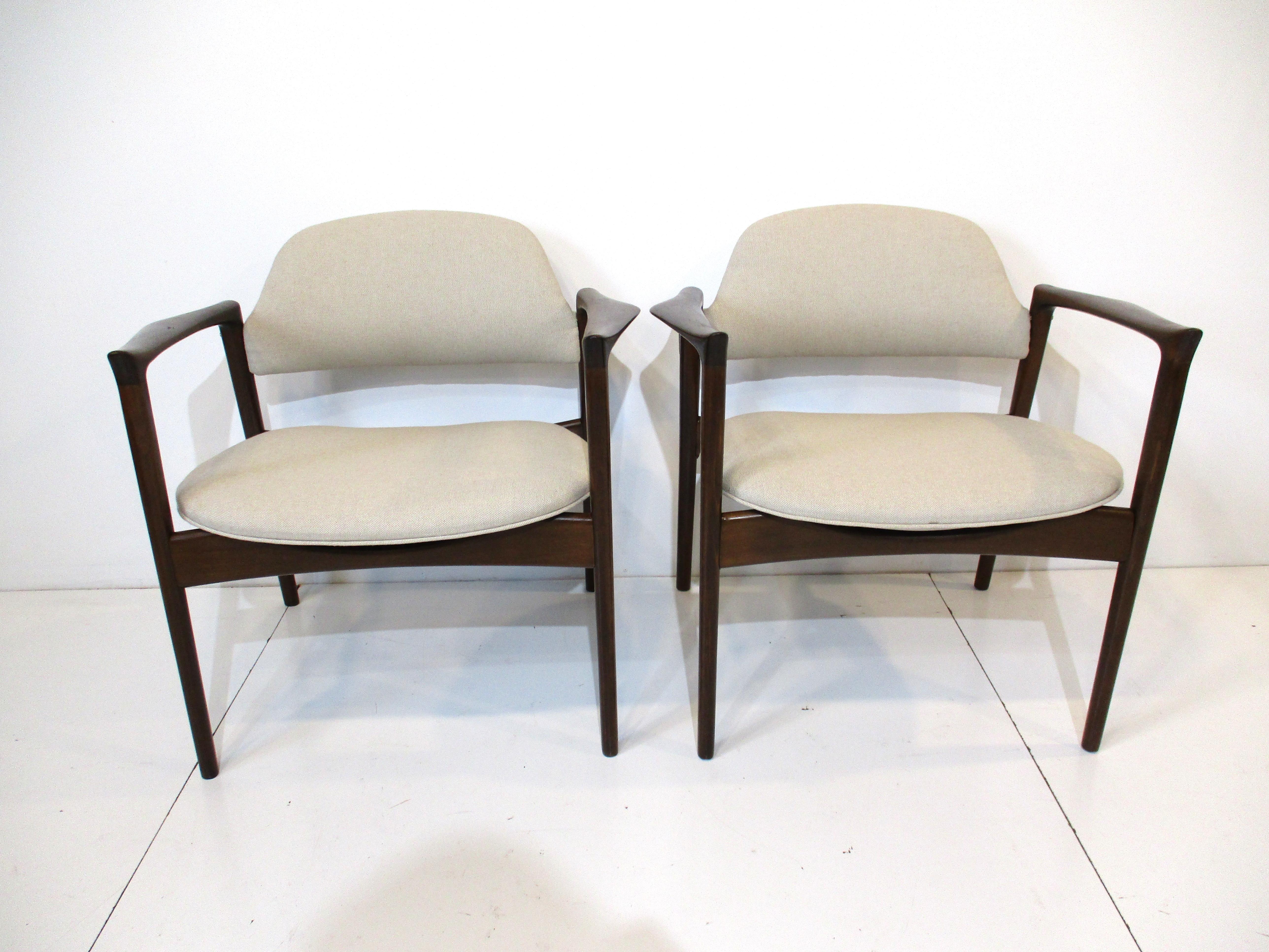 A pair of rare Ib Kofod Larsen writing lounge chairs with sculptural winged arms and very well crafted frames. Finished in a medium dark ebony with brass hardware and upholstered in a sand toned tightly woven linen blended fabric typical of Danish