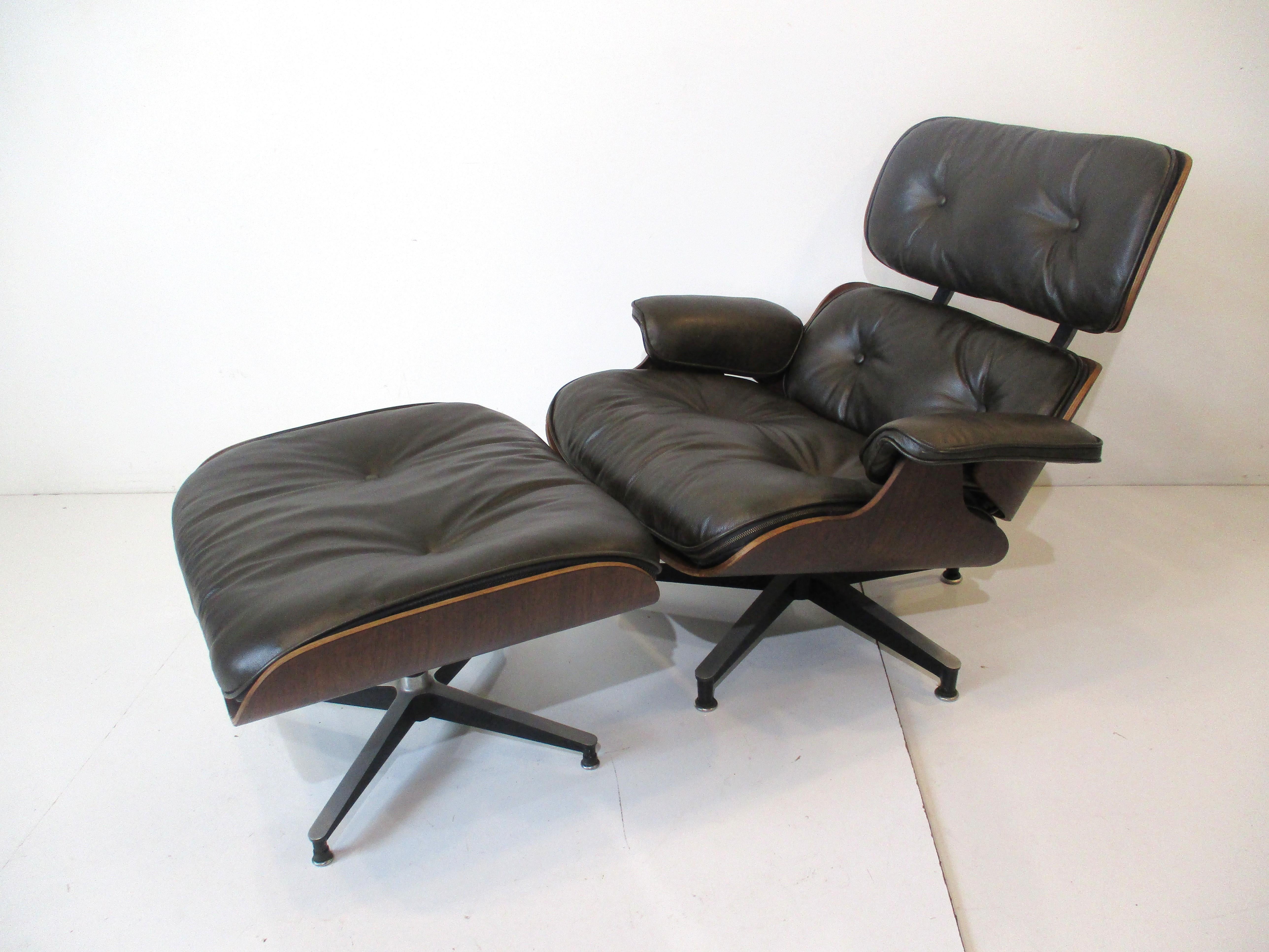 Un rare fauteuil de salon Eames 670 en cuir vert foncé avec ottoman assorti dans une salle d'exposition.  palissandre brésilien foncé et riche. Posé sur des bases en étoile en aluminium moulé avec des détails noirs, c'est l'icône du design et du