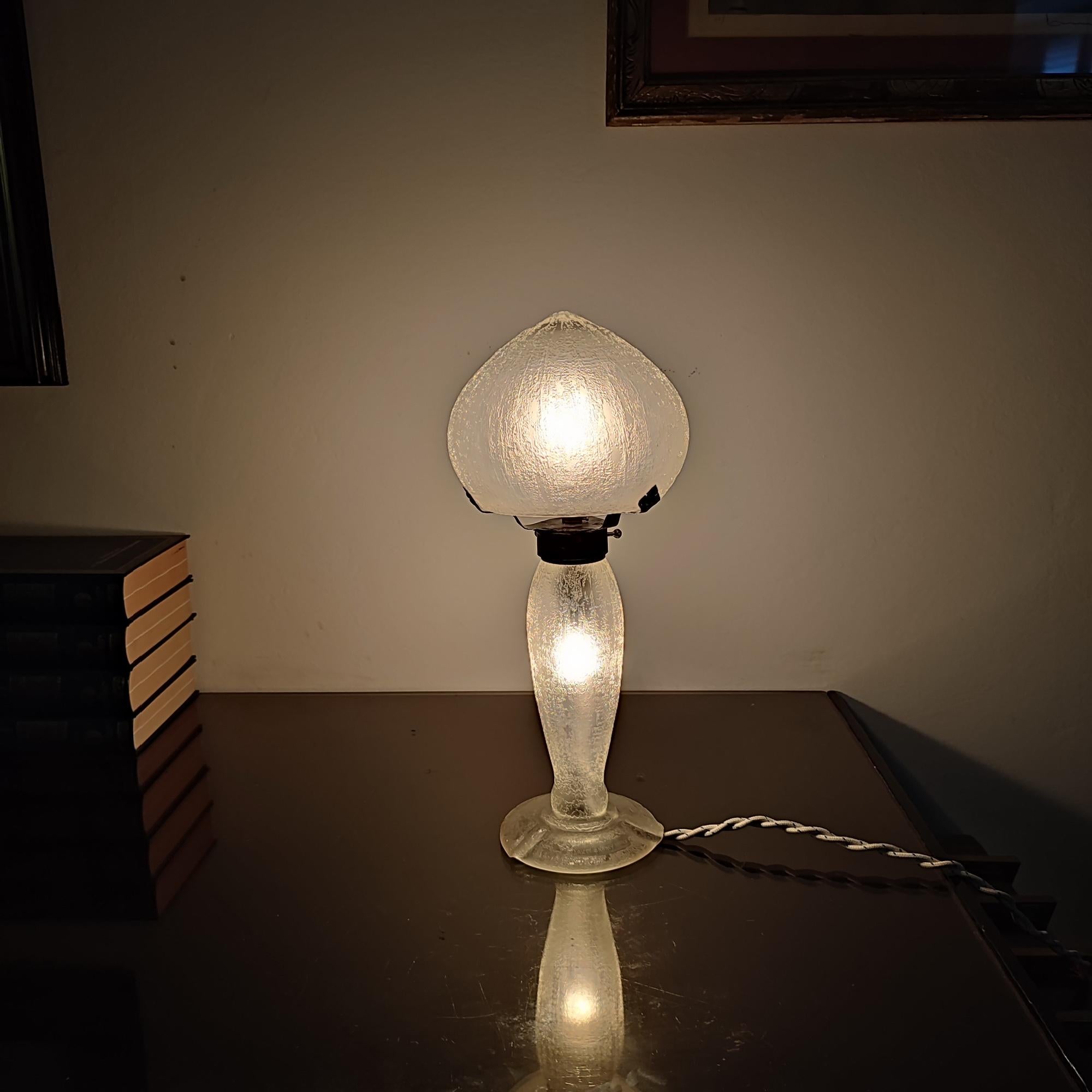 Lámpara de sobremesa Daum Nancy, Art Déco, Francia, años 30. Cristal ahumado incoloro, mate de hielo grabado. Tres brazos de hierro forjado martillado que sujetan la pantalla. Electrificado, pie iluminado. Pie y pantalla de lámpara con firma al