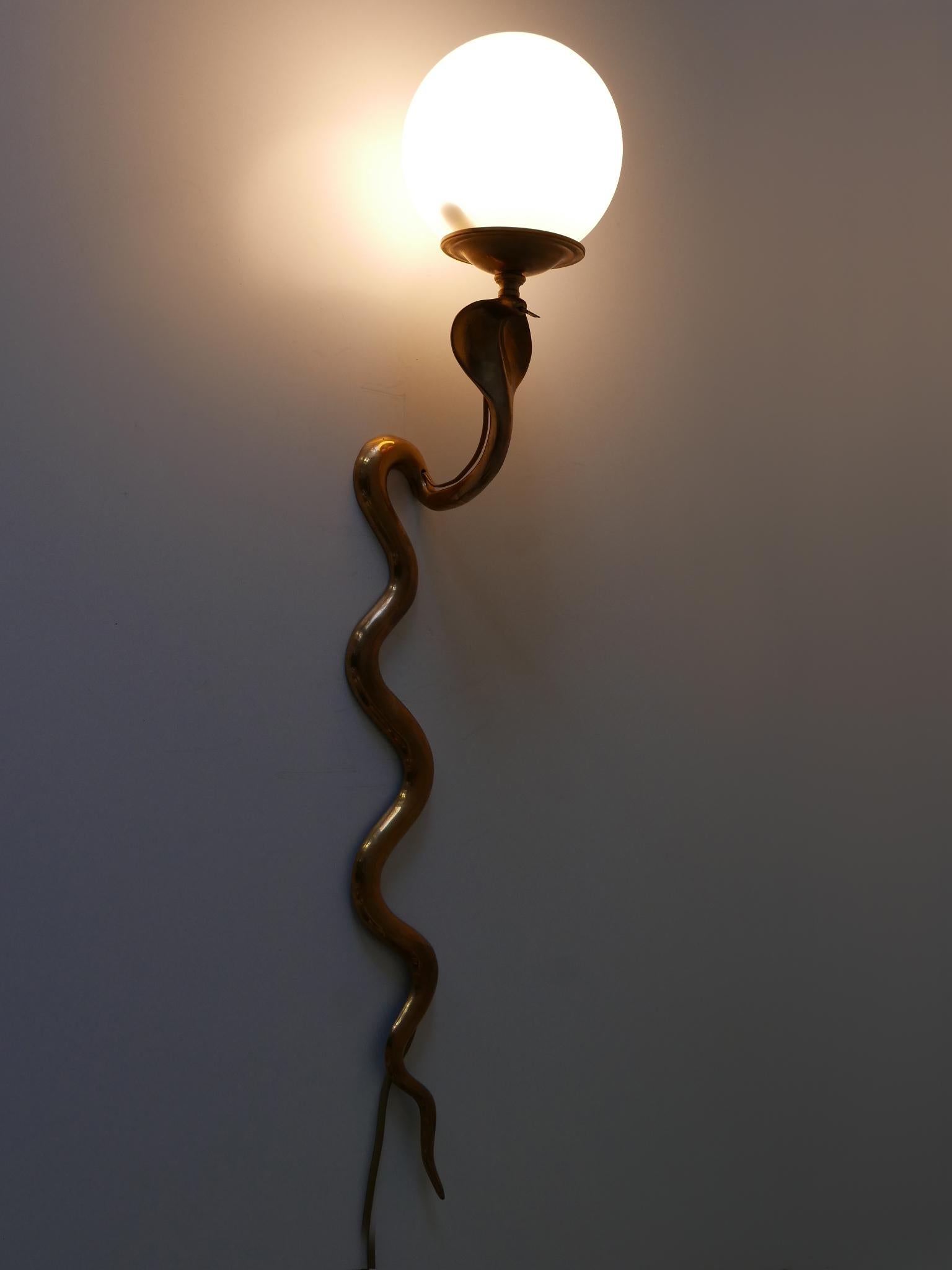Rare and elegant Mid-Century Modern cast brass cobra sconce or wall lamp, probably retailed by Maison Jansen. High quality item.

Executed in cast brass and opaline glass shade, the sconce needs 1 x E27 / E26 Edison screw fit bulb holder, is