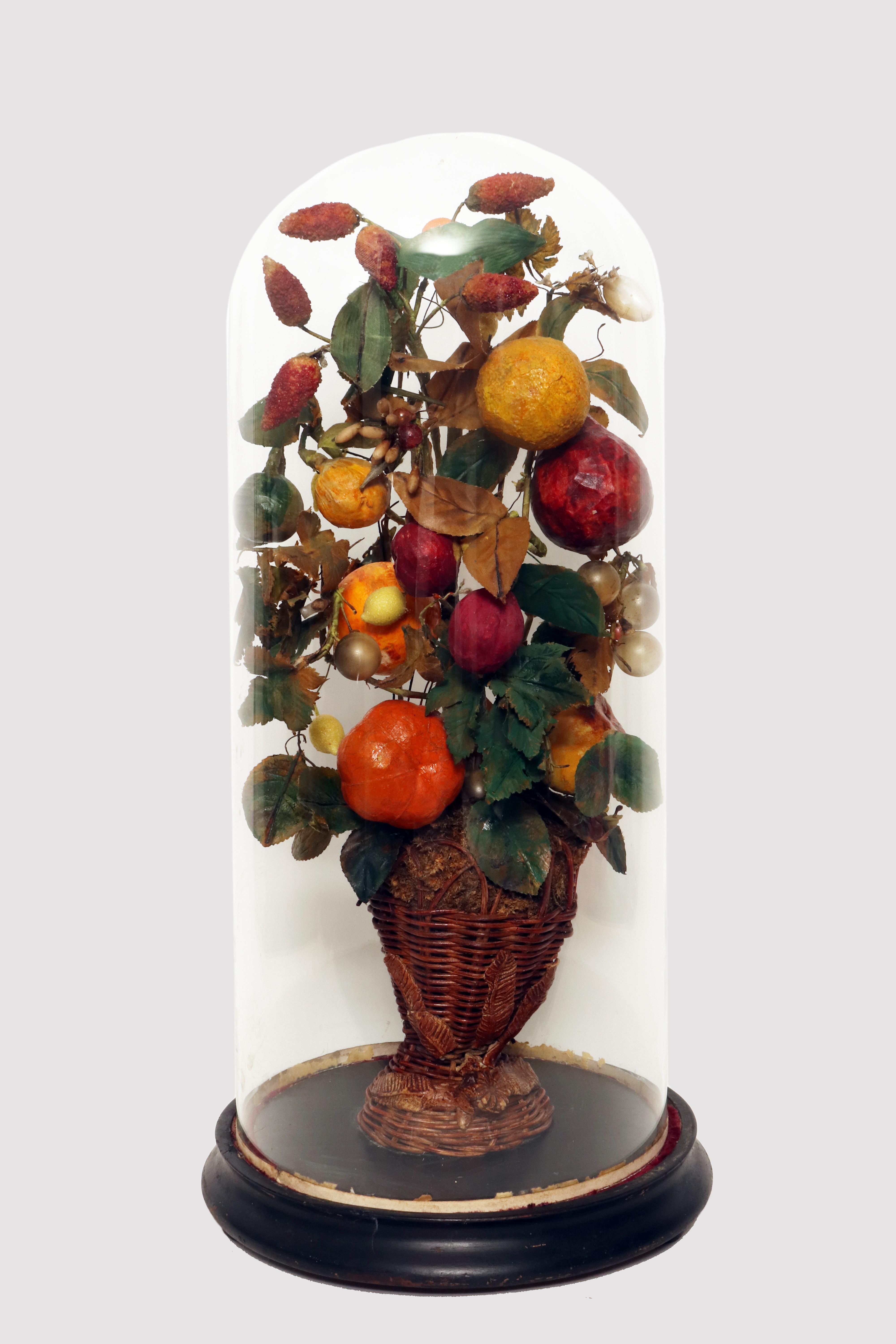 Composición que representa una cesta de mimbre en forma de jarrón con un triunfo decorativo de frutas hecho de cera. La elegante cesta de mimbre contiene un arreglo de frutas de cera de colores. Las ramas y las hojas están hechas de alambre, papel y