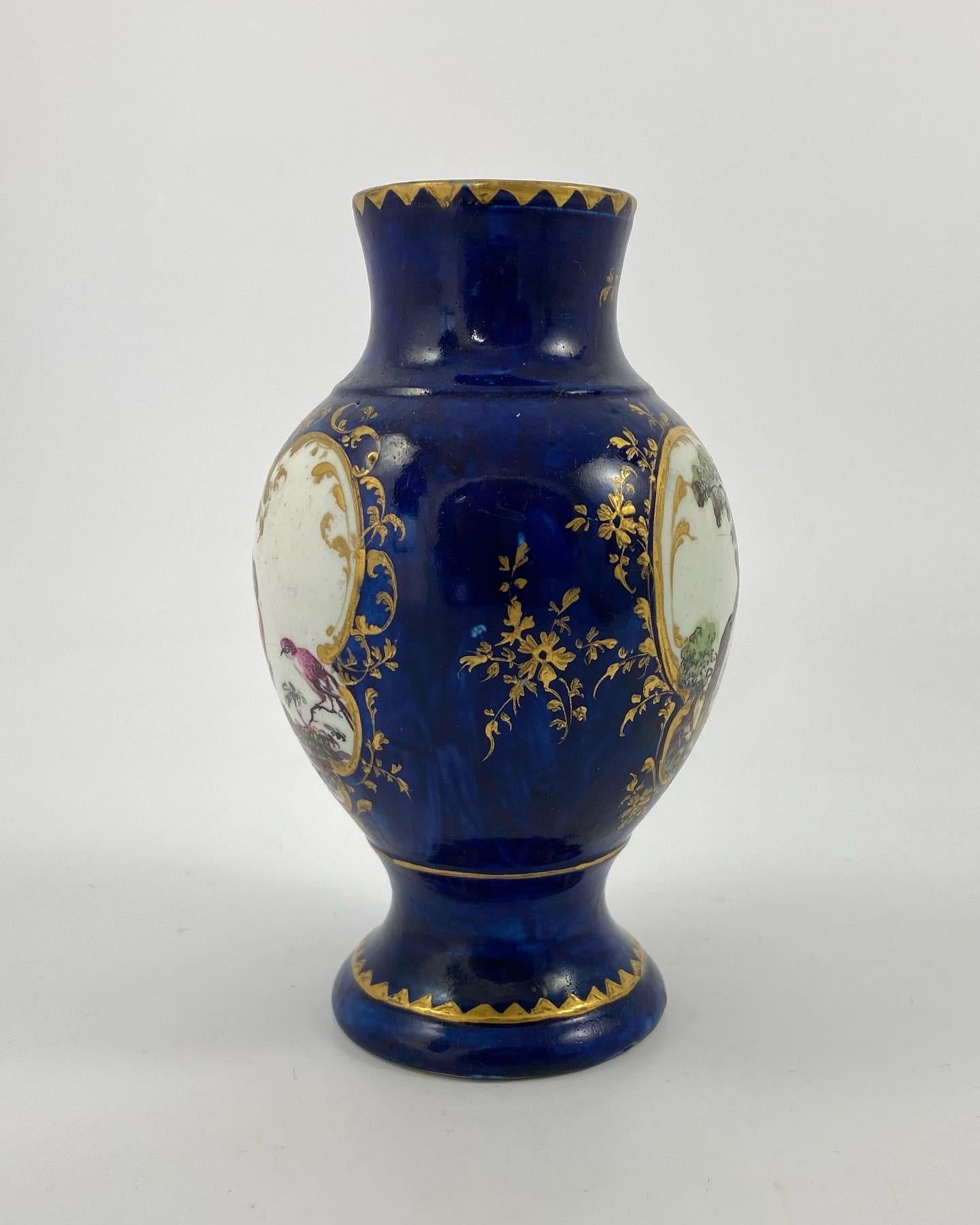 A rare Derby porcelain ‘Mazarine Blue’ vase, c. 1758. The vase, hand painted with a figure before a farm scene, within a shaped panel, edged in gilt floral scroll. The reverse, with a similar panel, painted with exotic birds. Further gilded sprays