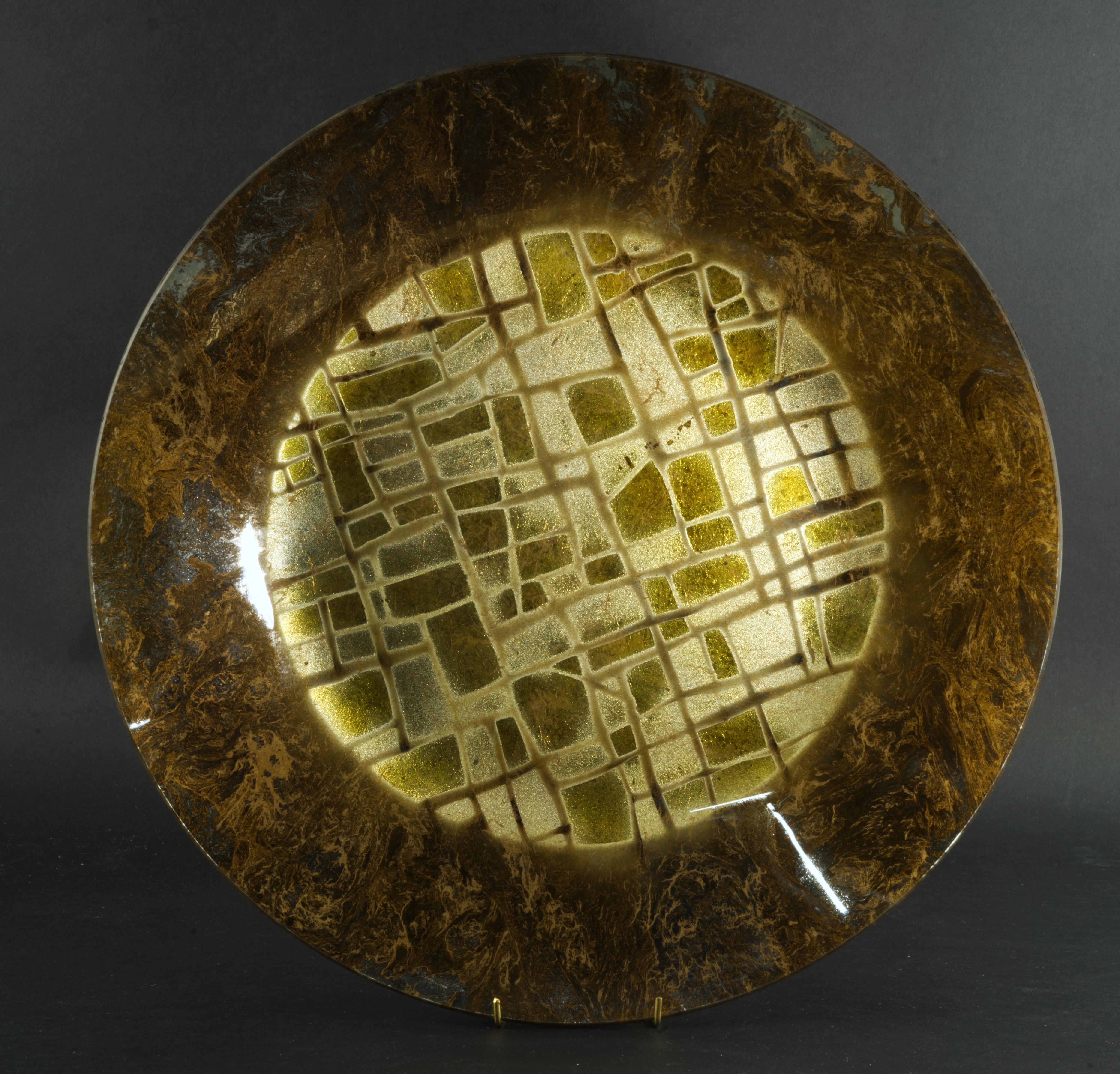 
Der seltene Glasteller oder die Schale wurde in den 1950er Jahren von Dick Talbett für sein Studio Ancient Glass als Teil der Radiant Temple-Serie handgefertigt. Die Schale zeigt in der Mitte ein abstraktes grafisches Muster in Gold und Silber, das