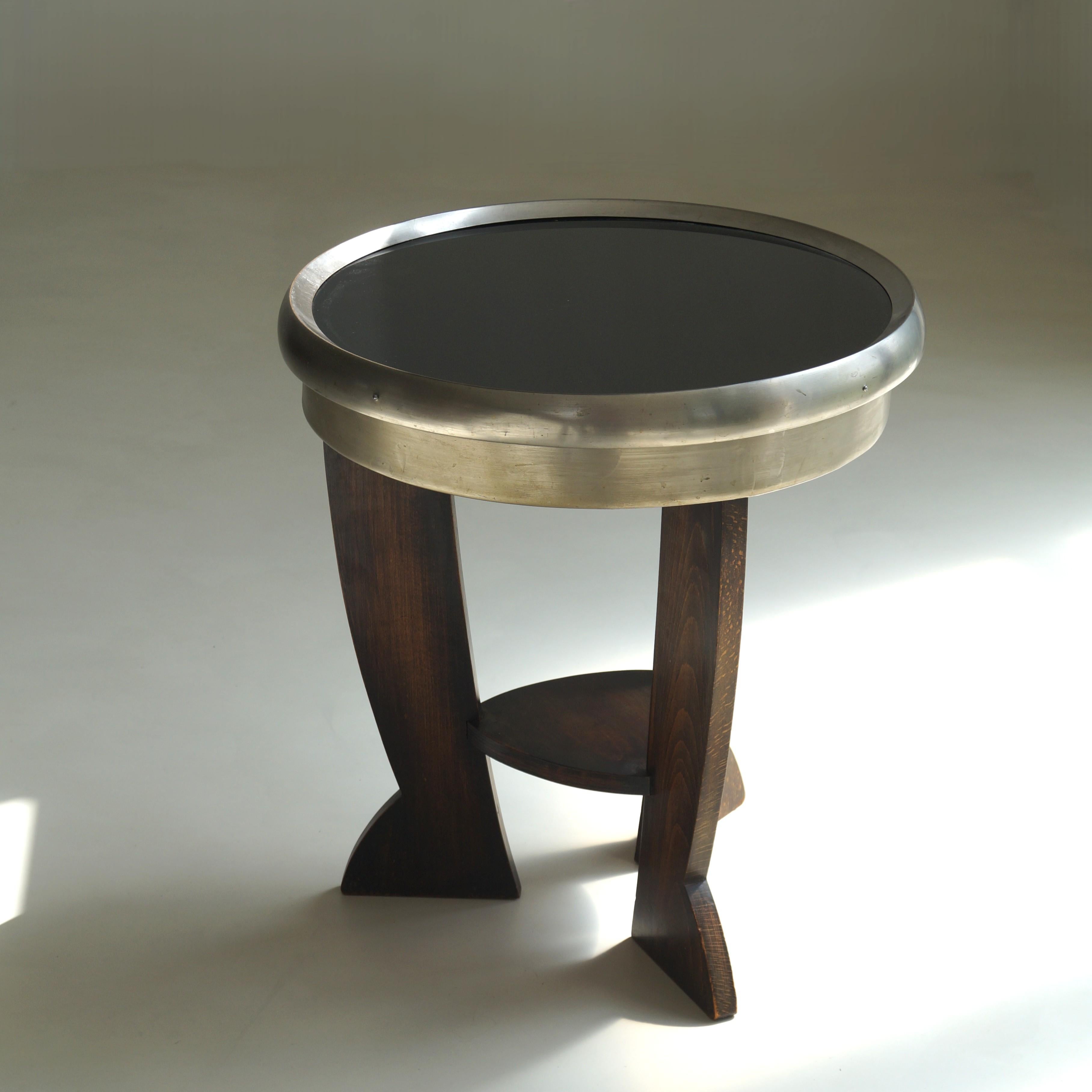 Elegante ed eccentrico tavolino a treppiede olandese Art Deco/Bauhaus con piano in vetro nero pece  con cornice in metallo e base scultorea in legno.
Le tre gambe in legno si svasano in estremità capricciose, simili a piedi, conferendo al tavolo un