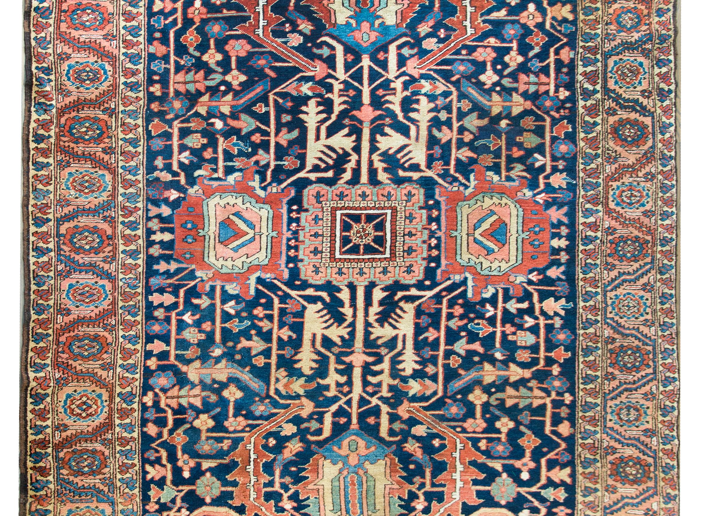 A rare and gorgeous early 20th century Persian Heriz rug with an unusual pattern containing two different large-scale stylized flowers connected with scrolling vines and living amidst a field of densely woven stylized vines and flowers, and all