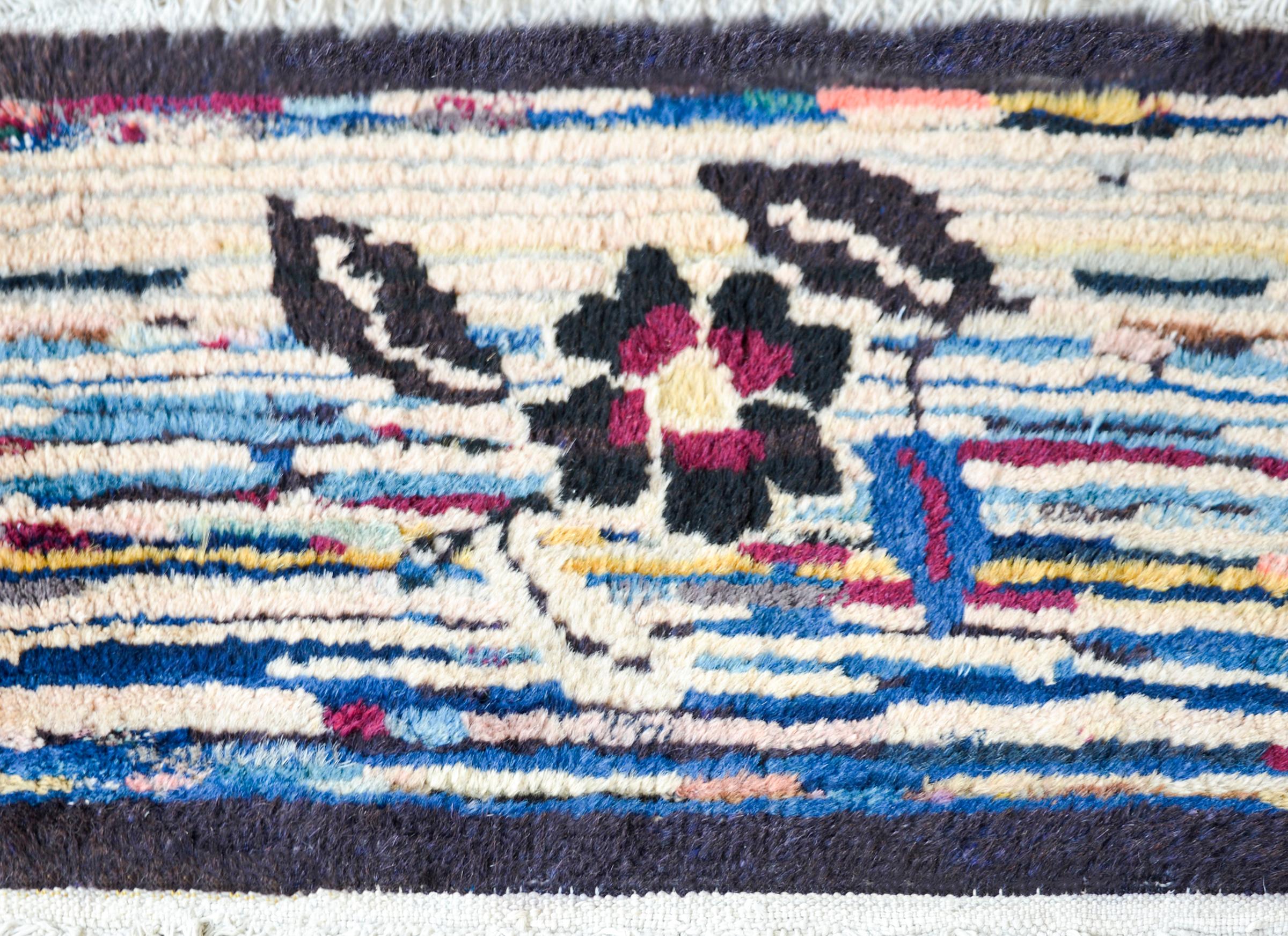 A rare early 20th century Tibetan rug with a single central peony against a multi-colored striped background and surrounded by a thick black border.