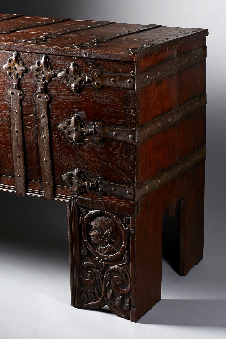 The large rectangular standing chest with full-height stiles, extensively mounted with wrought ironwork straps with quatrefoil finials which 'wrap' around the chest edges. These are fixed with convex head nails: running vertically up the front six