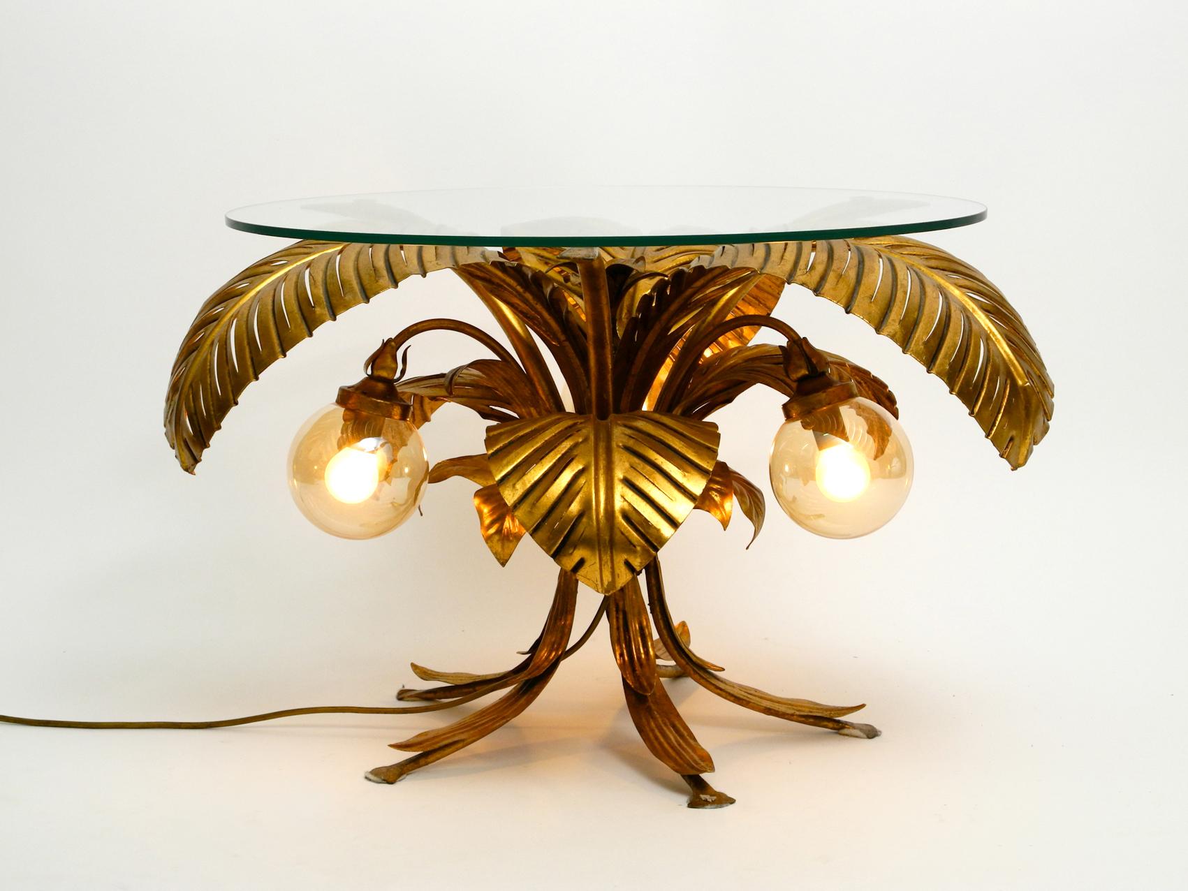 Very rare elegant illuminated 1980s Florentine table with original glass top.
Great unusual design with large leaves from an Italian production.
Completely made of metal, all gilded or elaborately painted in brass color.
Thick light tinted