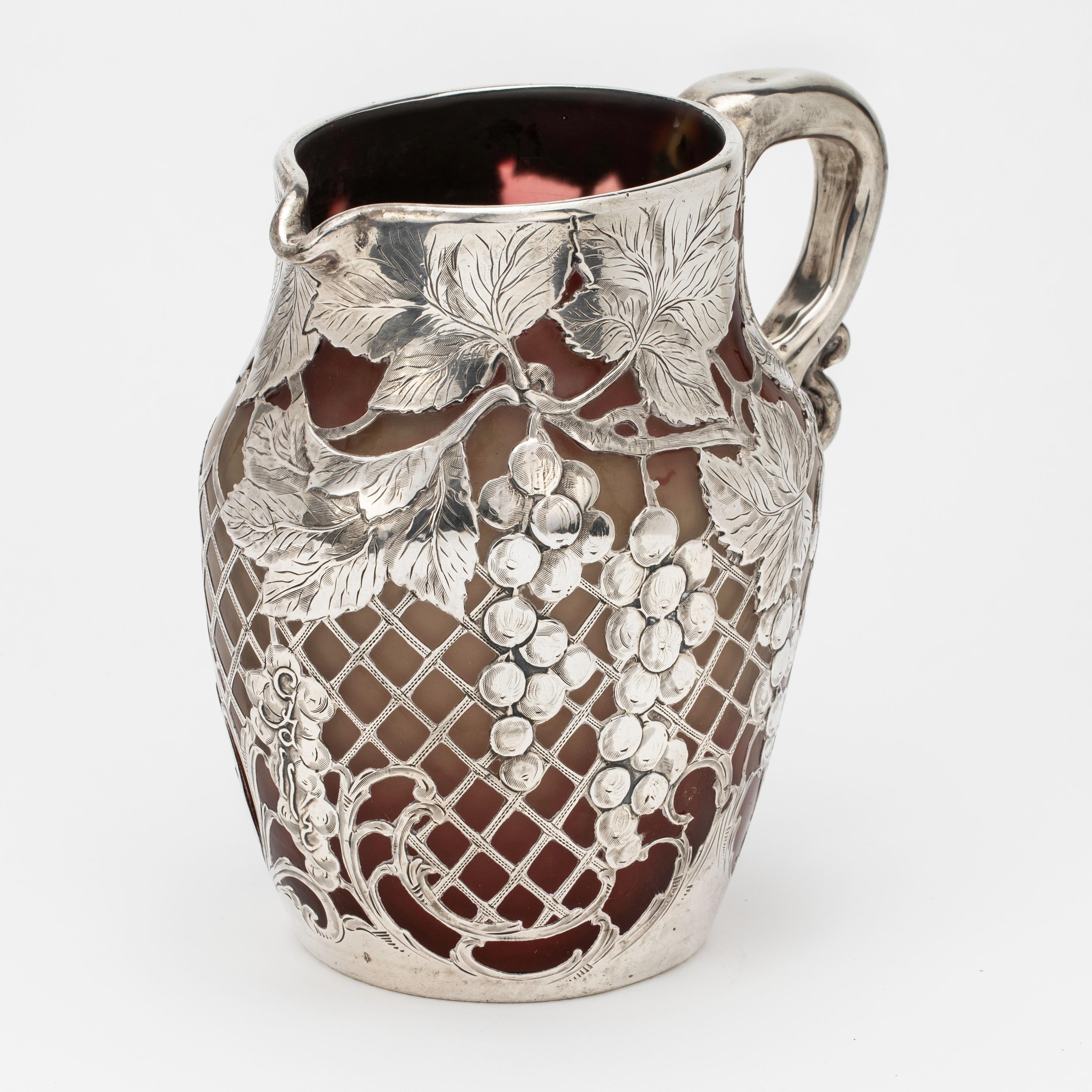 Beautiful Emile Galle glass pitcher in burgundy mottle glass, with sterling silver overlay in grape motif. Galle signature hallmark on the grape silver motif, and Alvin silver hallmark at the base of the pitcher. “ b b “ etched at the bottom of the
