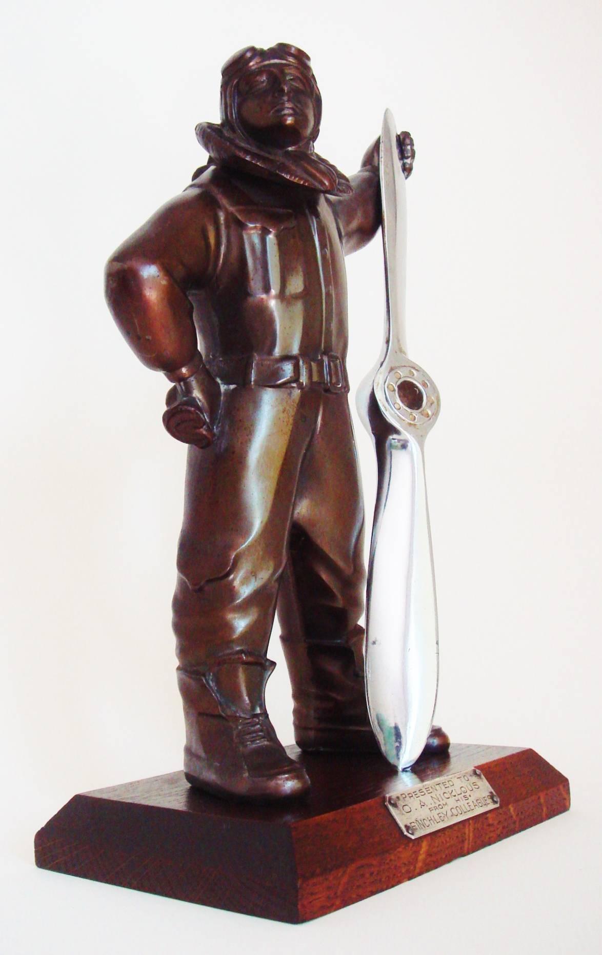 This very rare, all original English Art Deco chrome and bronzed spelter pilot wheel and flint table lighter is mounted on a chamfered mahogany base that bears a silver plated presentation plaque. The heroic looking pilot has a faux bronze finish