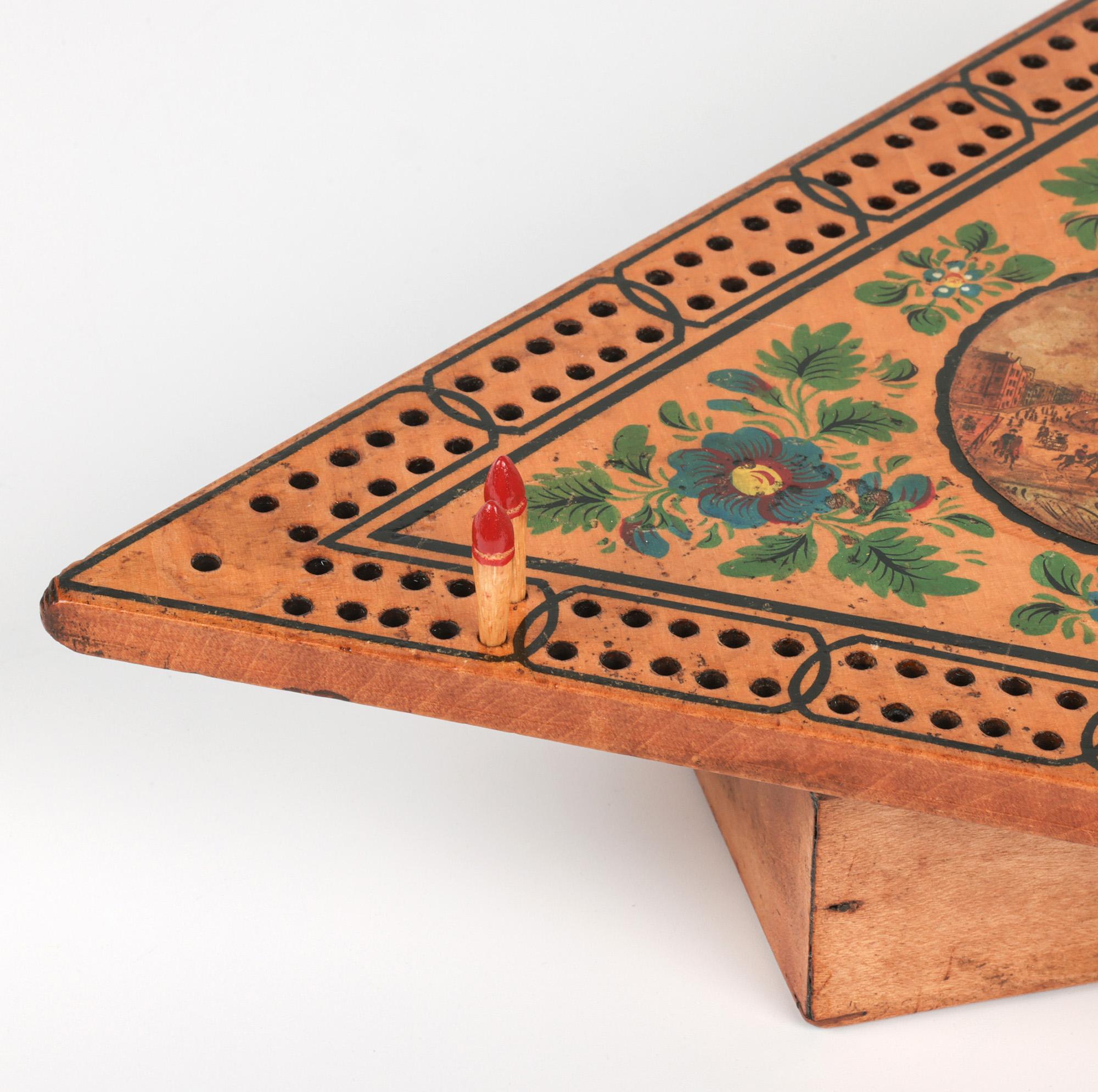 Raro tablero de juego inglés de madera para cribbage con una vista de Bristol que data del reinado de Jorge IV, 1820 a 1830. El tablero, de forma triangular, está montado sobre una base en forma de caja con una original tapa corredera sencilla, cuyo