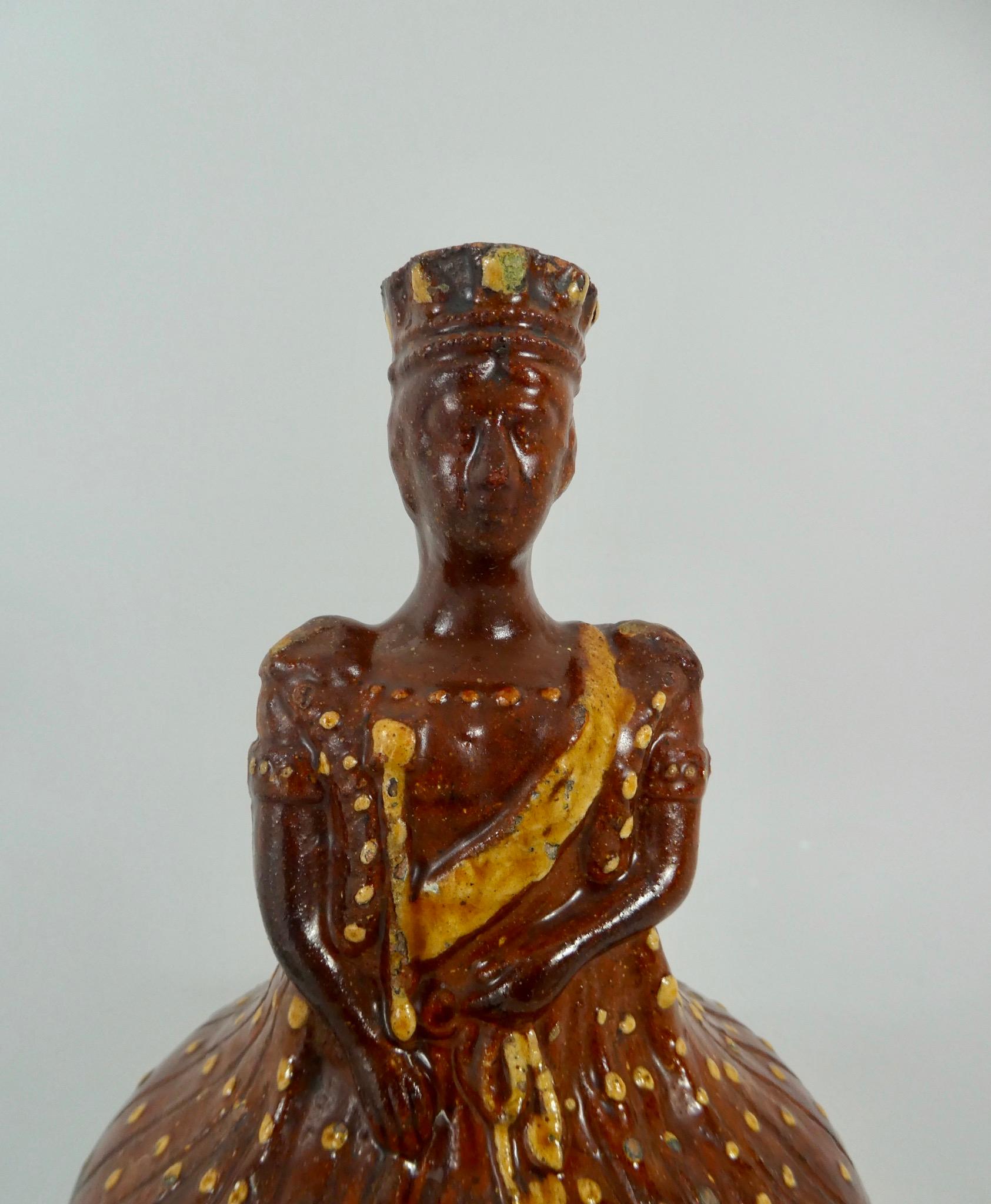 A very rare English pottery slipware flask, circa 1837. Made to commemorate the Coronation of Queen Victoria, after a painting by Sir George Haytor. Modelled with her majesty’s head forming the neck of the flask, and her voluminous gown, the body of