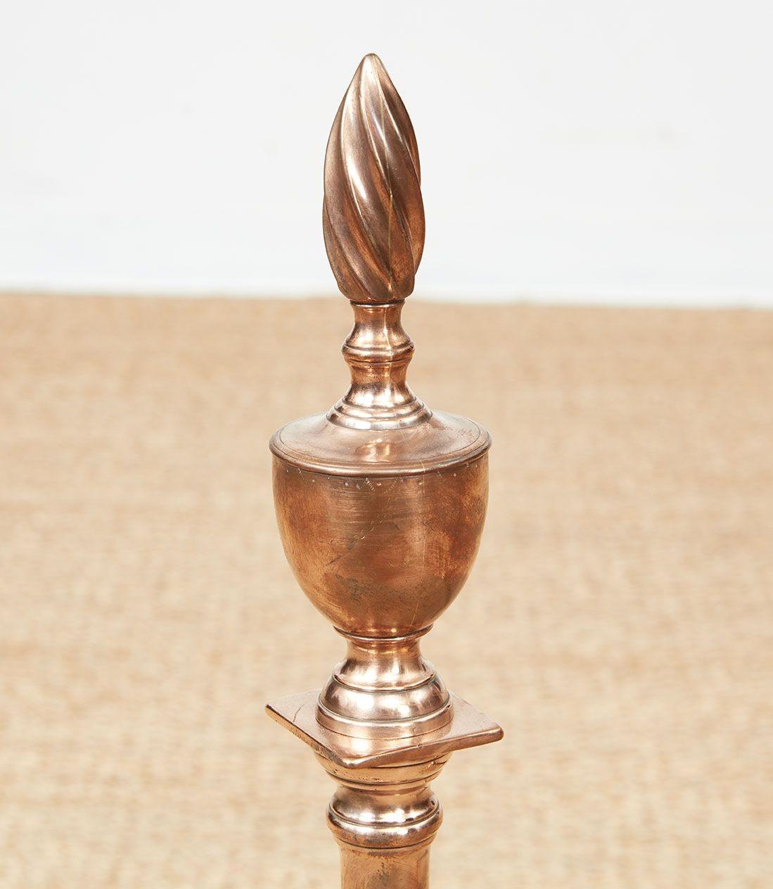 Very rare American classical bell metal andirons having flaming urn finials over column shafts and standing on square plinths over arched spurred legs ending in ball and claw feet, all with engraved decoration.  Probably Philadelphia, circa 1780.