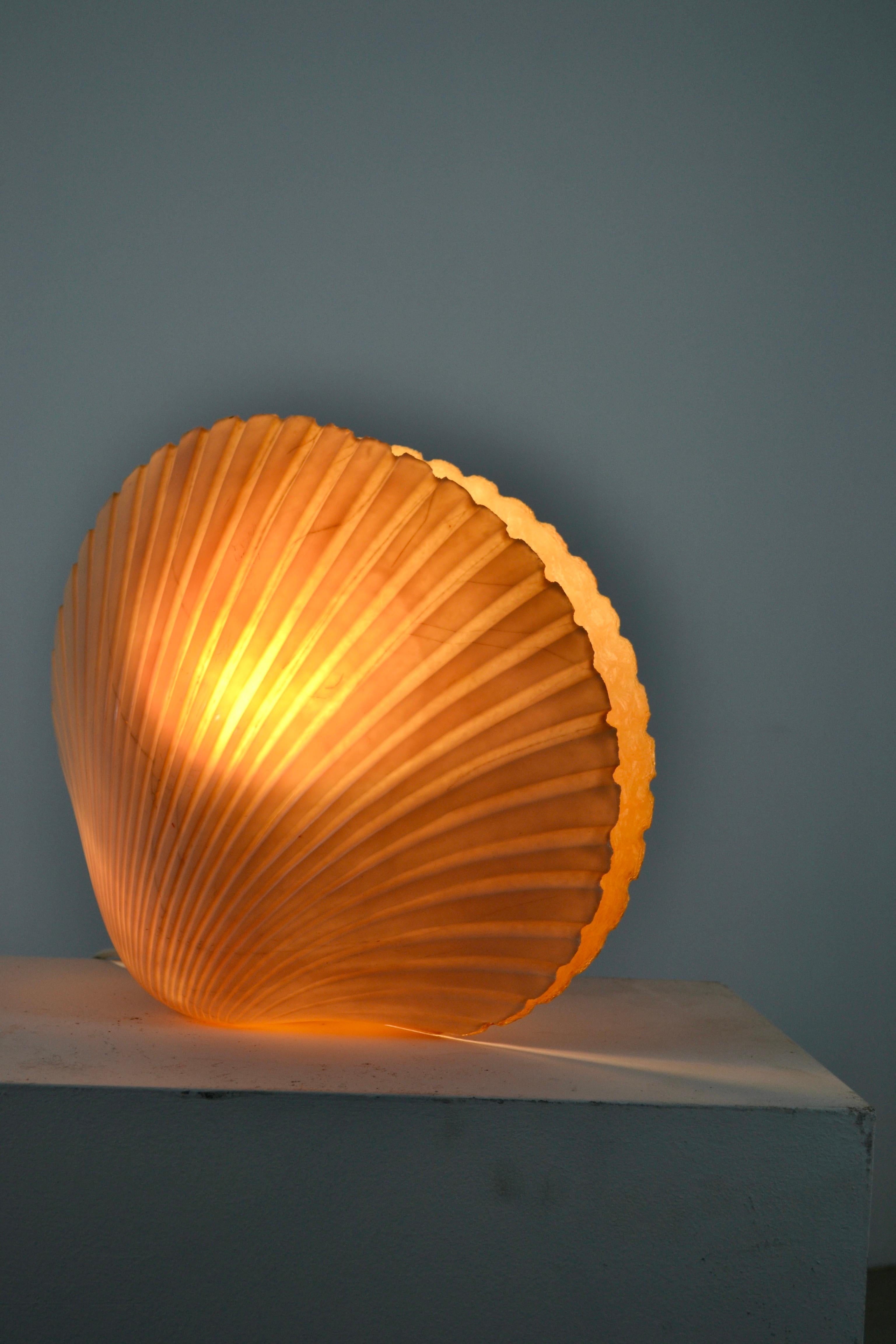 This handcrafted fiberglass lamp emits a soft, warm glow, creating an intimate and cozy atmosphere.

Its ingenious design allows for adjustable light intensity: the shell, mounted on a hinge, can be opened or closed to modulate the illumination as