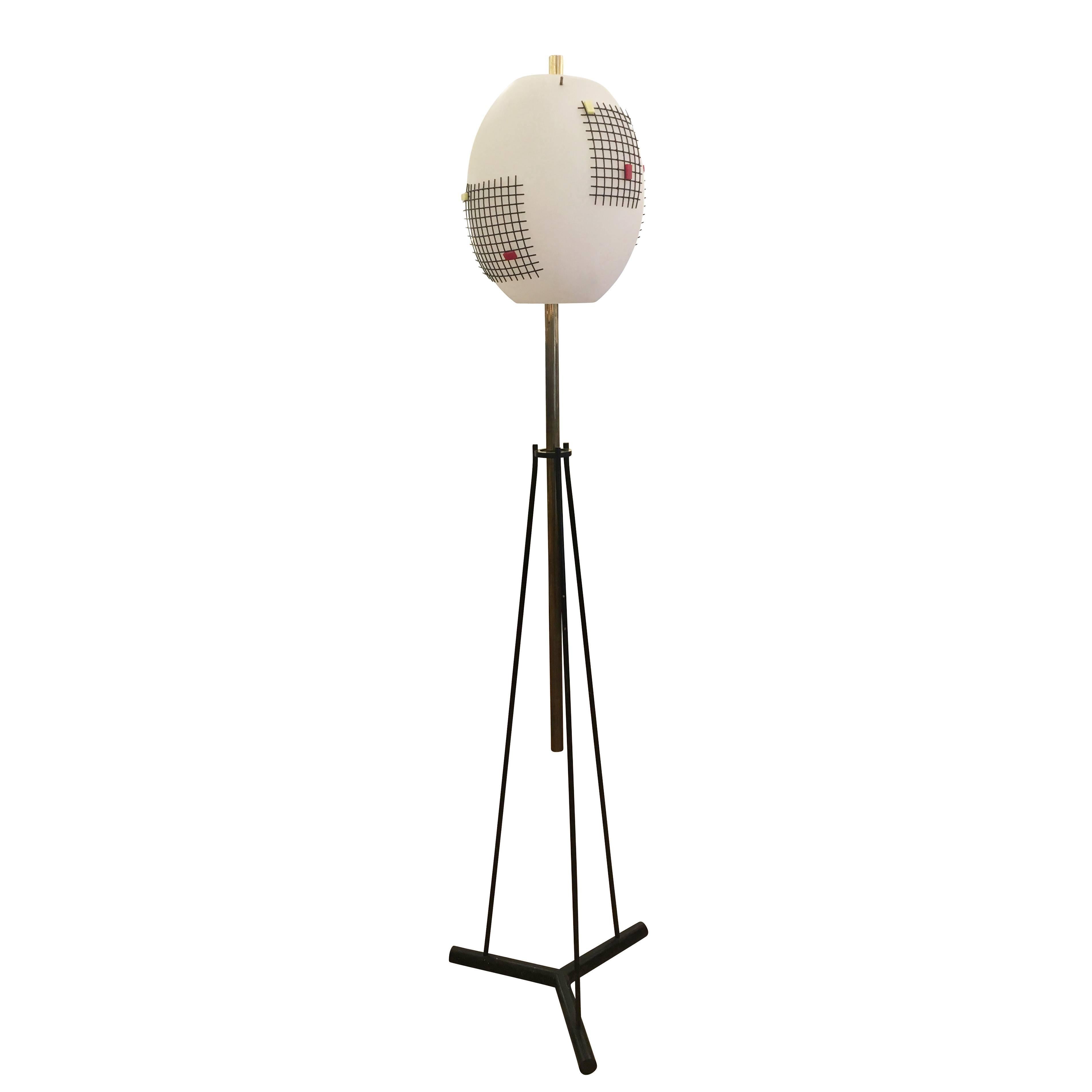 Rare floor lamp designed by Angelo Lelli for Arredoluce in the 1960s. Features a large oval glass shade on a tripod base. The shade is decorated with four black metal grids which are held in place by red and yellow perspex cubes. The base is