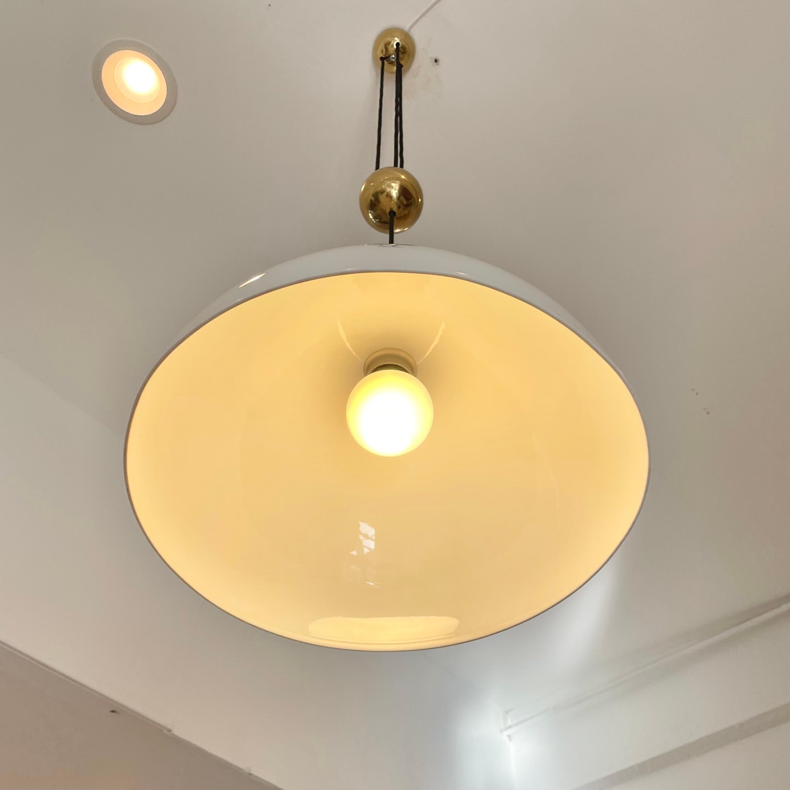 Rare counter balance pendant by Florian Schulz. Beautiful brass canopy feeds three black cloth cords with a centered brass counter balance ball. Ceramic shade in a soft cream color can be pulled down or pushed up to shorten or extend the length of