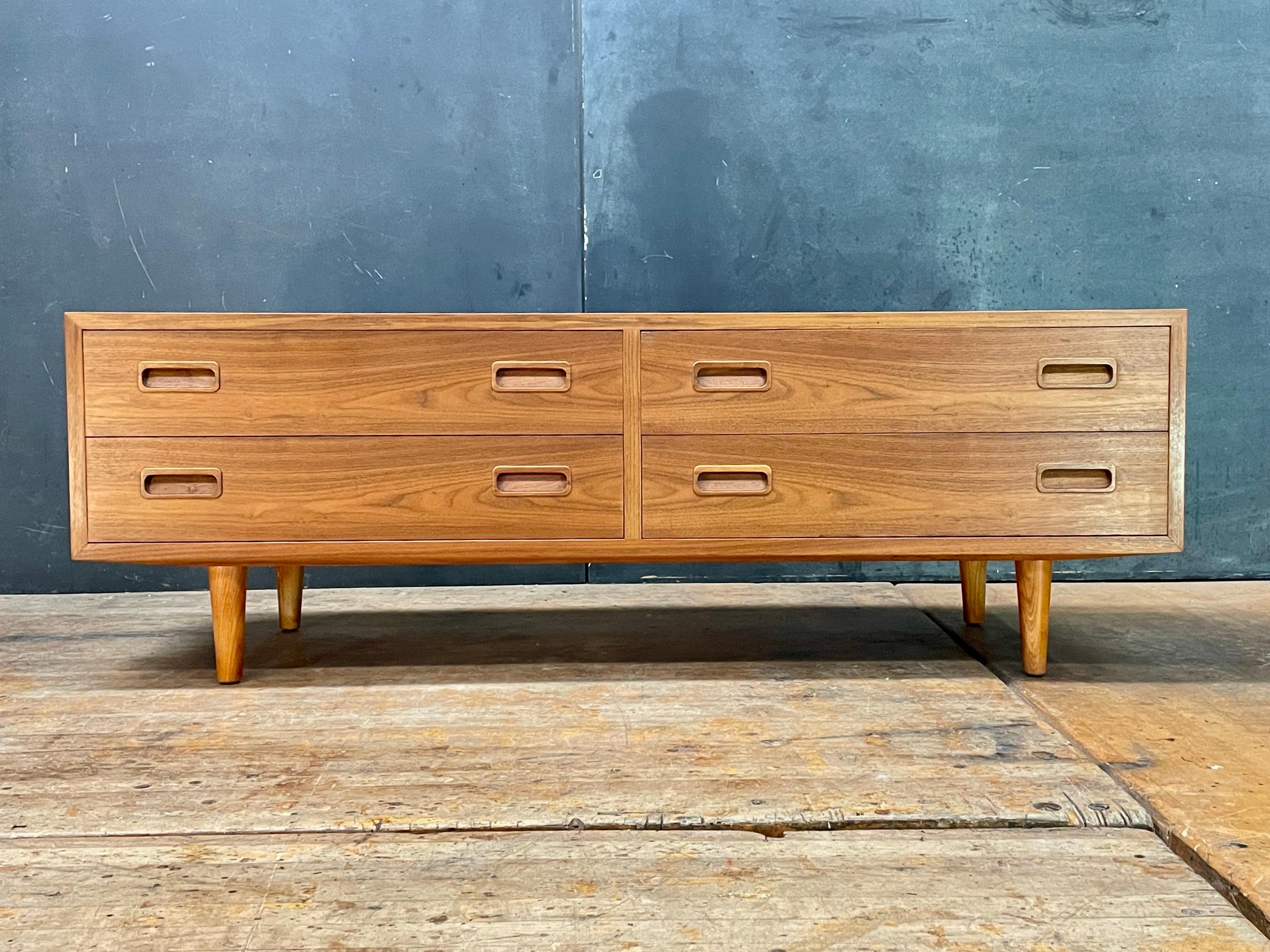 Uncommon low chest of drawers, with minimalist inset drawer pulls, and wonderful figured teak grain, bookmatched across the facing drawer surfaces. Smooth functioning drawers.

Measures: L 54.5 x D 16.88 x H 18.5 in.