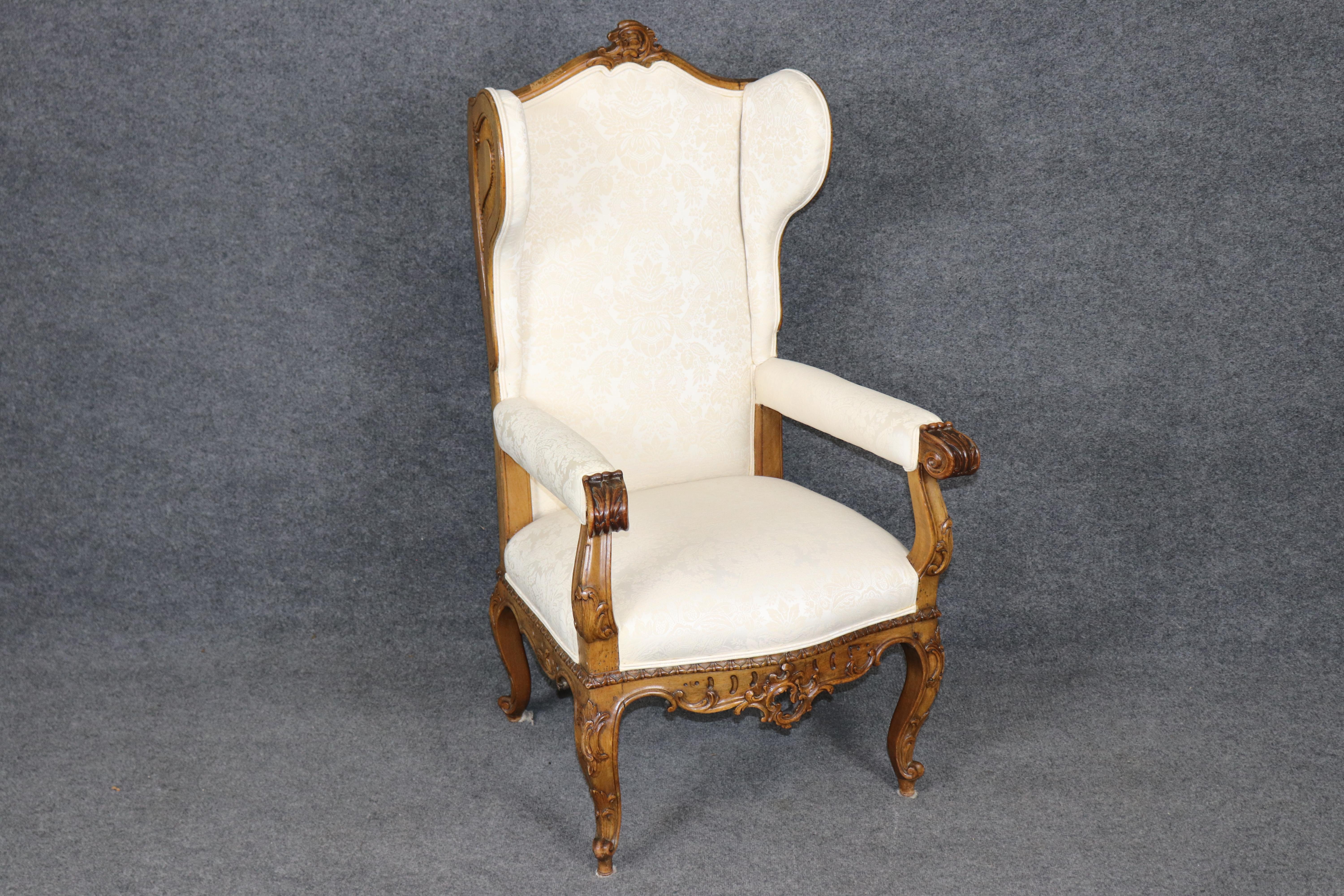 Dieser exquisite französische Ohrensessel im Stil Ludwigs XV. ist ein Beispiel für die Grandeur und Kunstfertigkeit des Rokoko-Designs. Der Stuhl mit seinem fein geschnitzten Nussbaumgestell zeigt geschwungene Kurven, Akanthusblattrollen und florale
