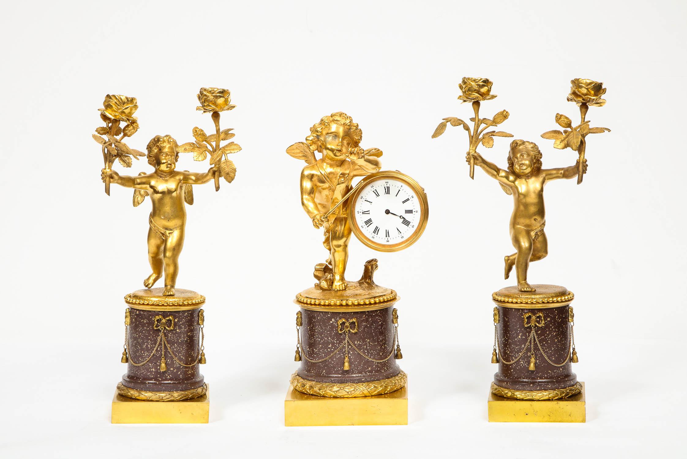 A rare French gilt-bronze ormolu and porphyry three-piece clock set,
circa 1880, possibly by Henry Dasson, Paris.

Comprising of a clock and a pair of candlesticks. All three with putti and porphyry. Very good quality.

Clock: 12.5