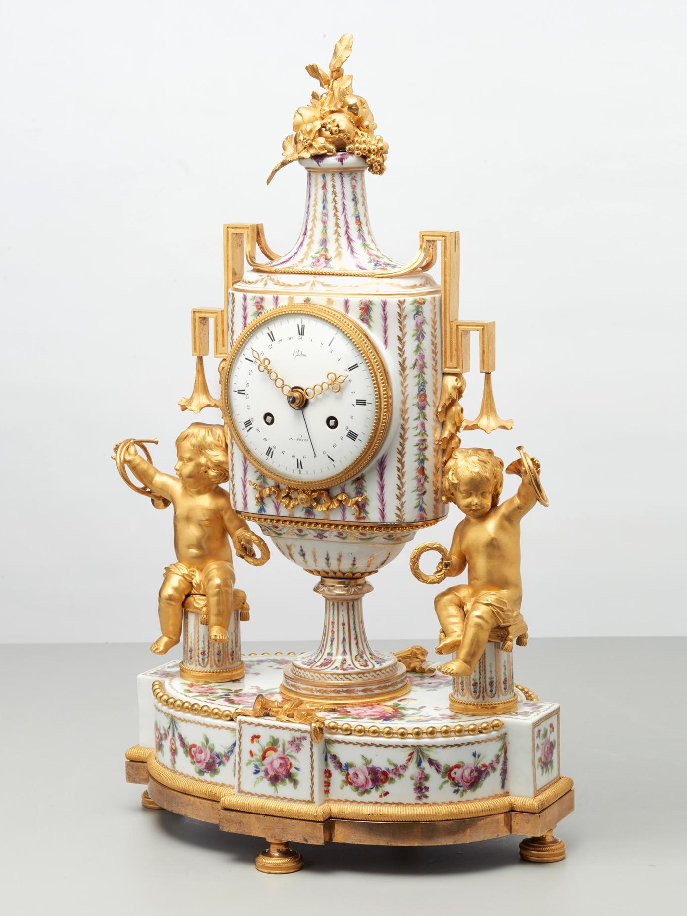 The enamel dial indicating the hours, minutes and date, bears the signature Godon a Paris. It is set in a footed vase of hard-paste Paris porcelain, with angular handles. Painted with delicate polychrome garlands, leaves and flowers, it rests on a