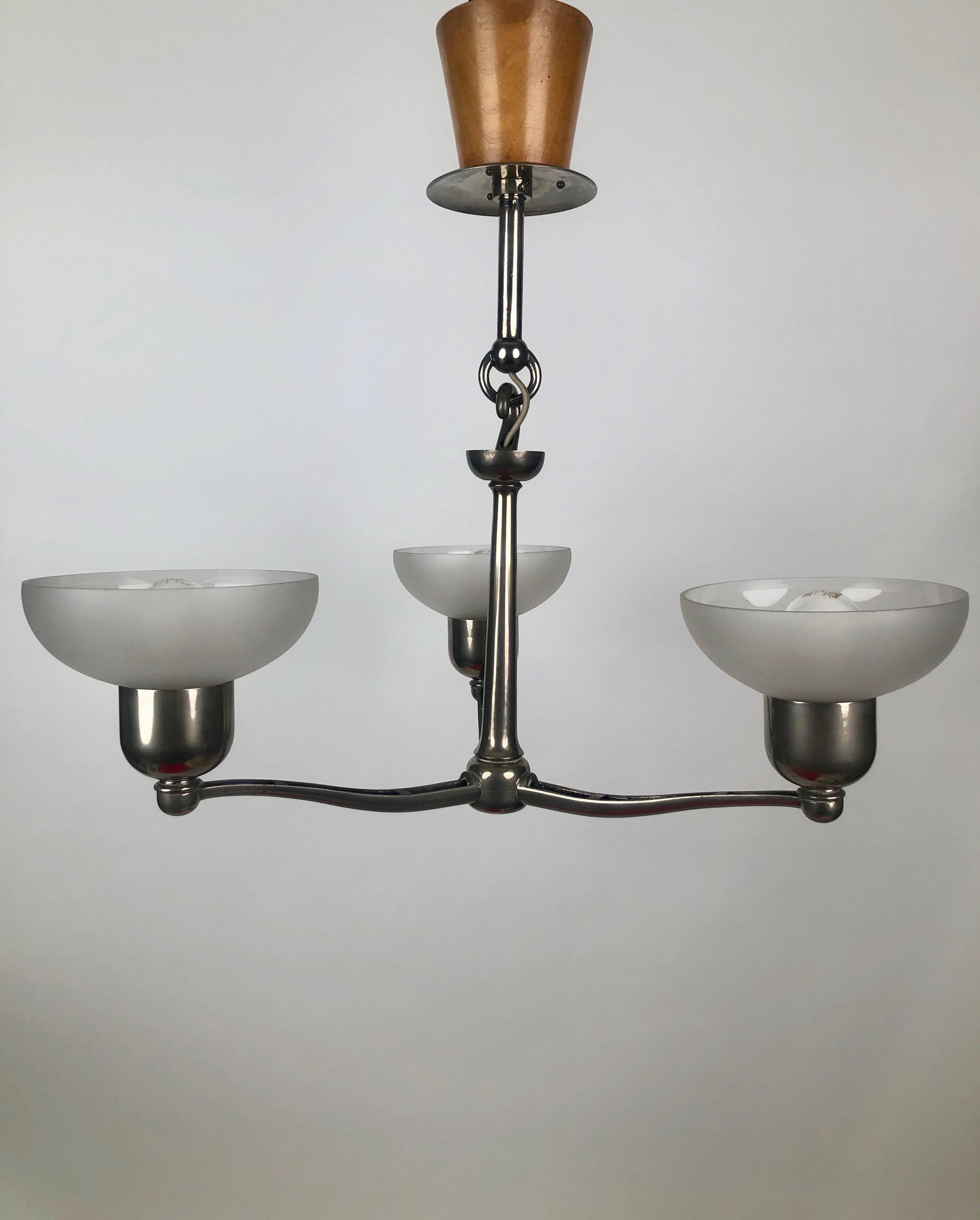 A functionalist three arm chandler from 1930, Austria.
The metal parts are made from cast aluminium with an unusual wooden canopy 
and three frosted glass shades.