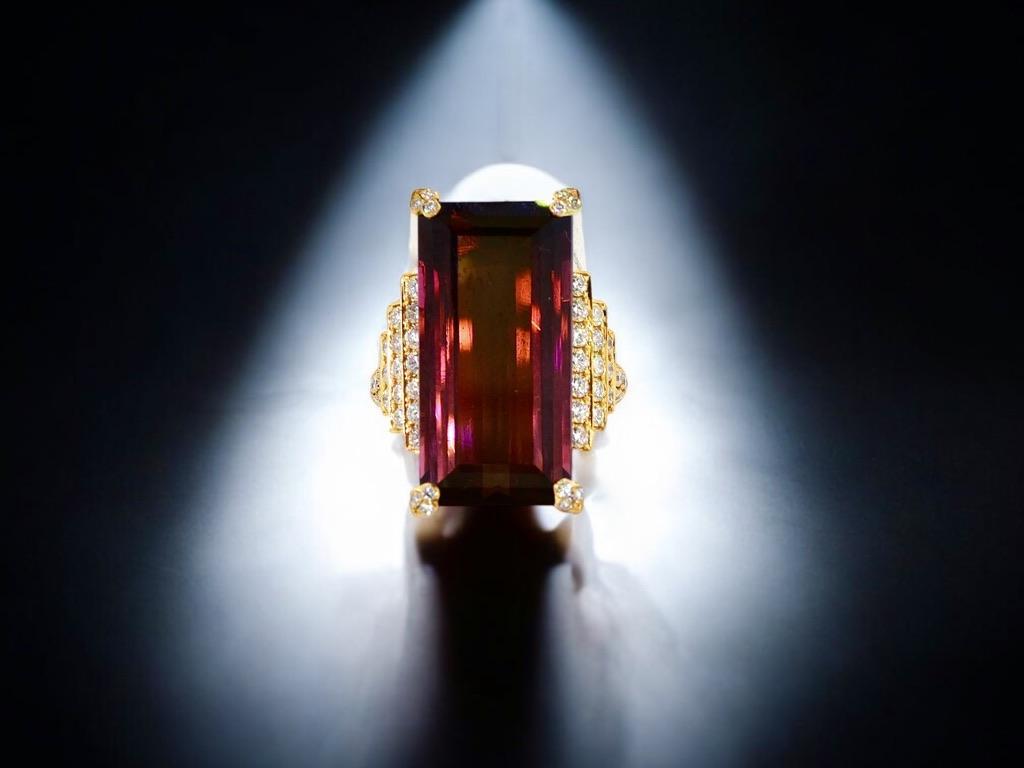 Rubelita natural fina, también llamada turmalina roja. Esta piedra es brillante, clara y presenta un color frambuesa vivo y profundo. Esta larguísima piedra de talla esmeralda está sujeta por cuatro garras engastadas cada una con 3 pequeños