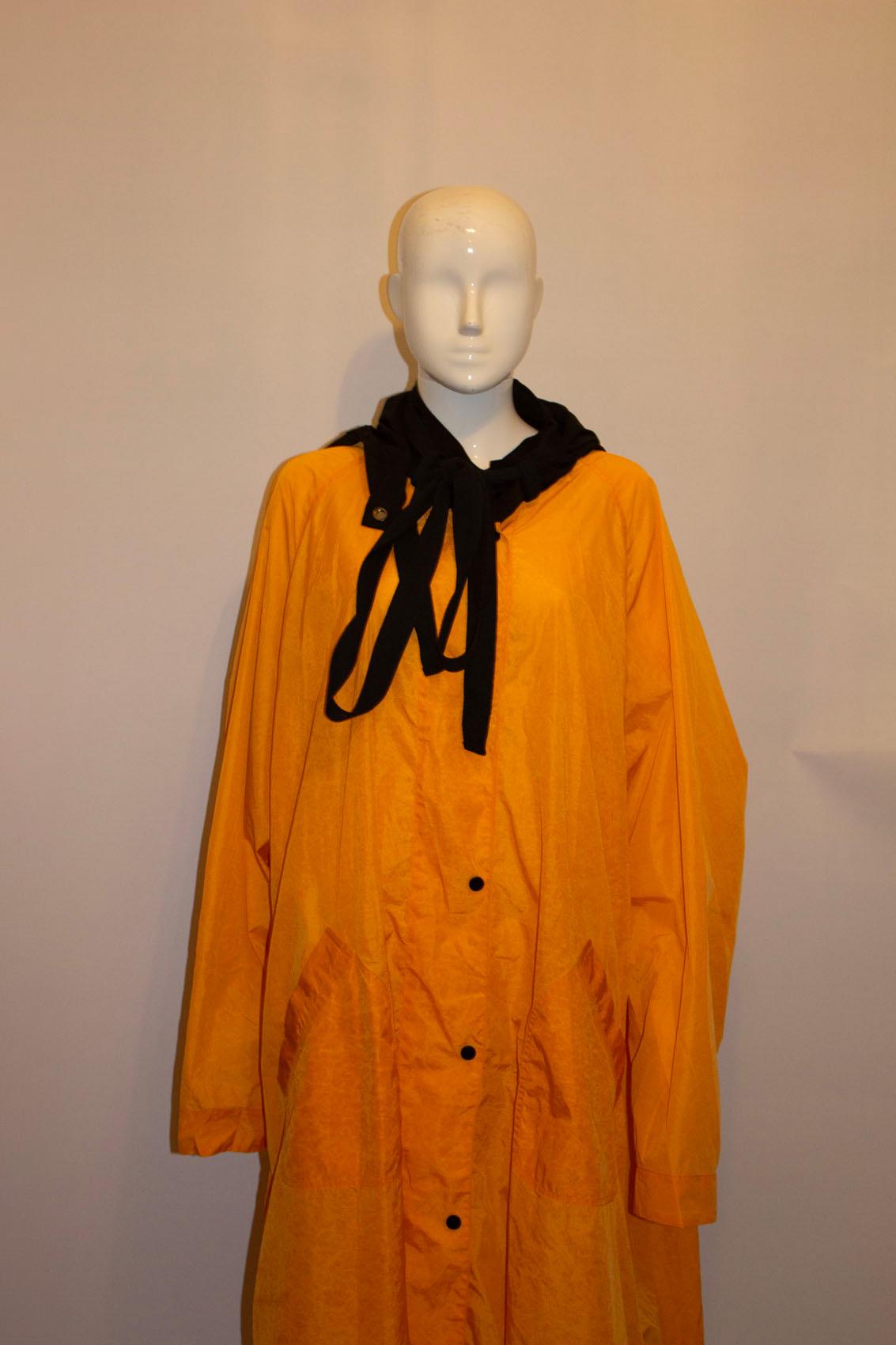 A rare festival or bad weather cover up from Alexander McQueen, In a great colour match of orange and black, the coat has a popper front fastening and two large front pockets.  It has a black collar and detachable black hood.  The hood can be stored