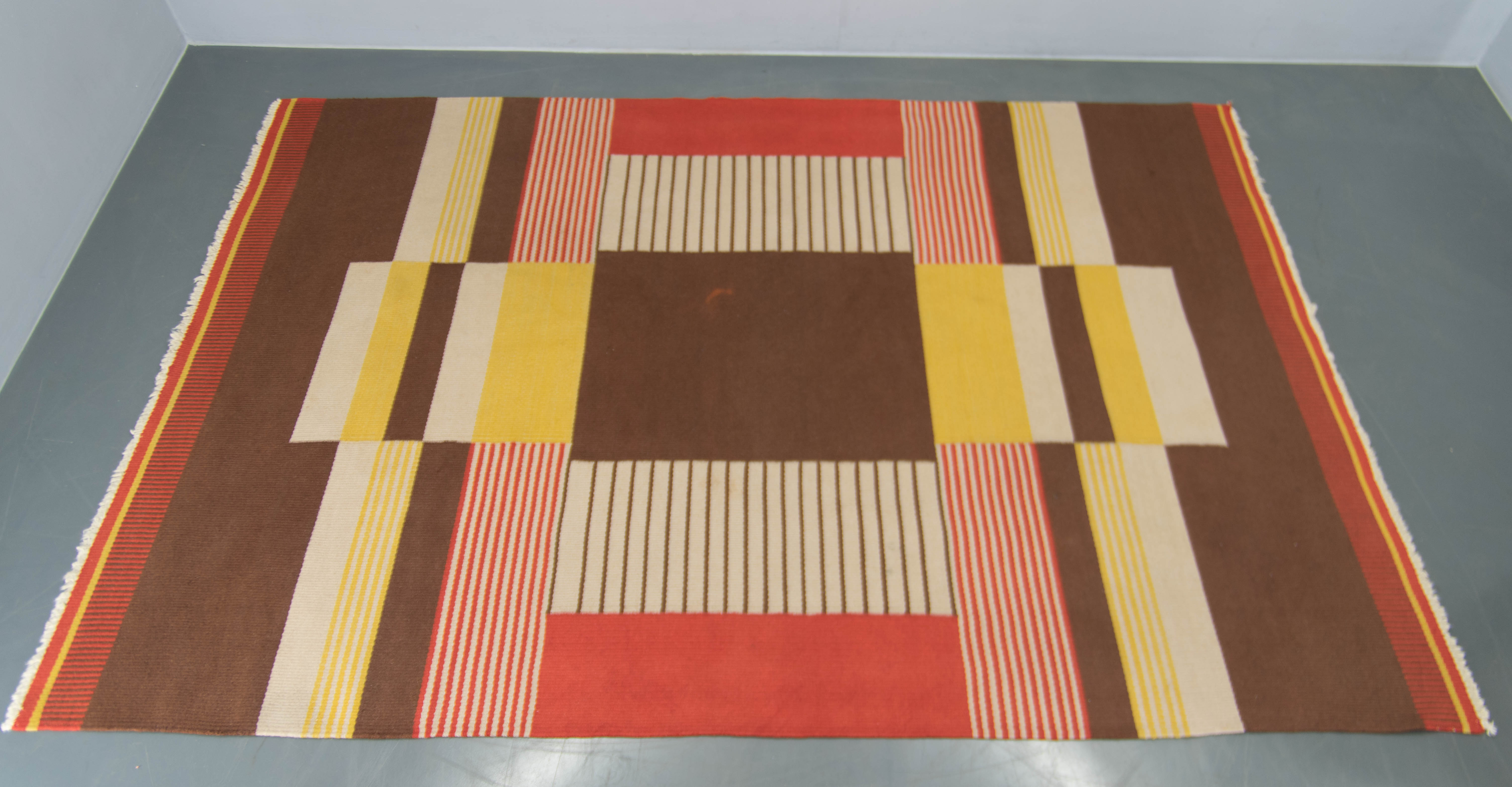 Dieser atemberaubende Vintage-Teppich von Antonin Kybal aus dem Jahr 1948 kombiniert kühne geometrische Muster mit einer warmen und einladenden Farbpalette aus tiefen Rot-, Braun-, Gelb- und Cremetönen. Das handgewebte Wolltextil zeigt ein perfektes