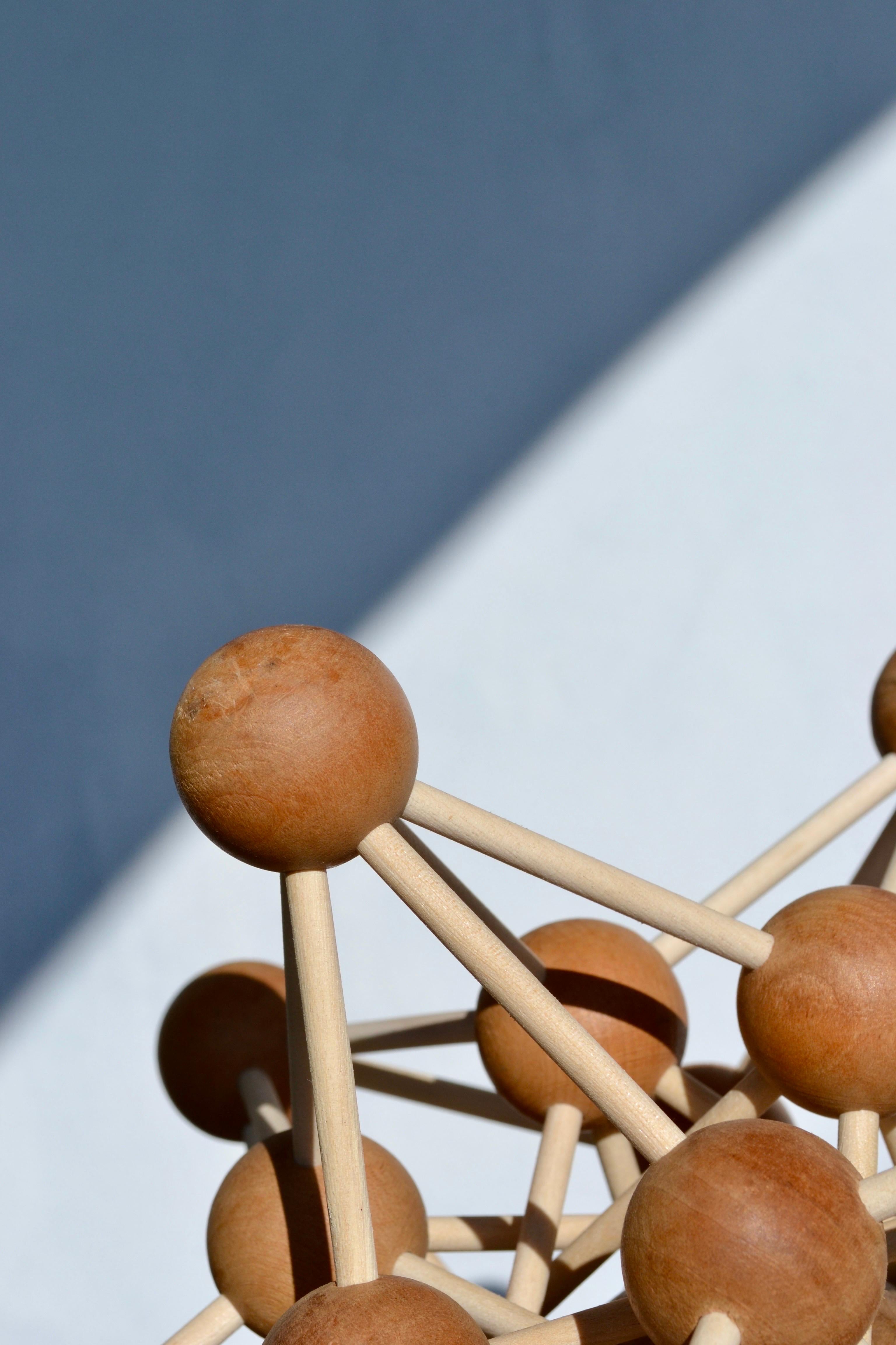 Esta excepcional escultura rompecabezas de madera sobredimensionada presenta una intrincada estructura geométrica de esferas y varillas entrelazadas, que forman un sorprendente diseño poliédrico. A la vez rompecabezas y obra de arte, encarna la