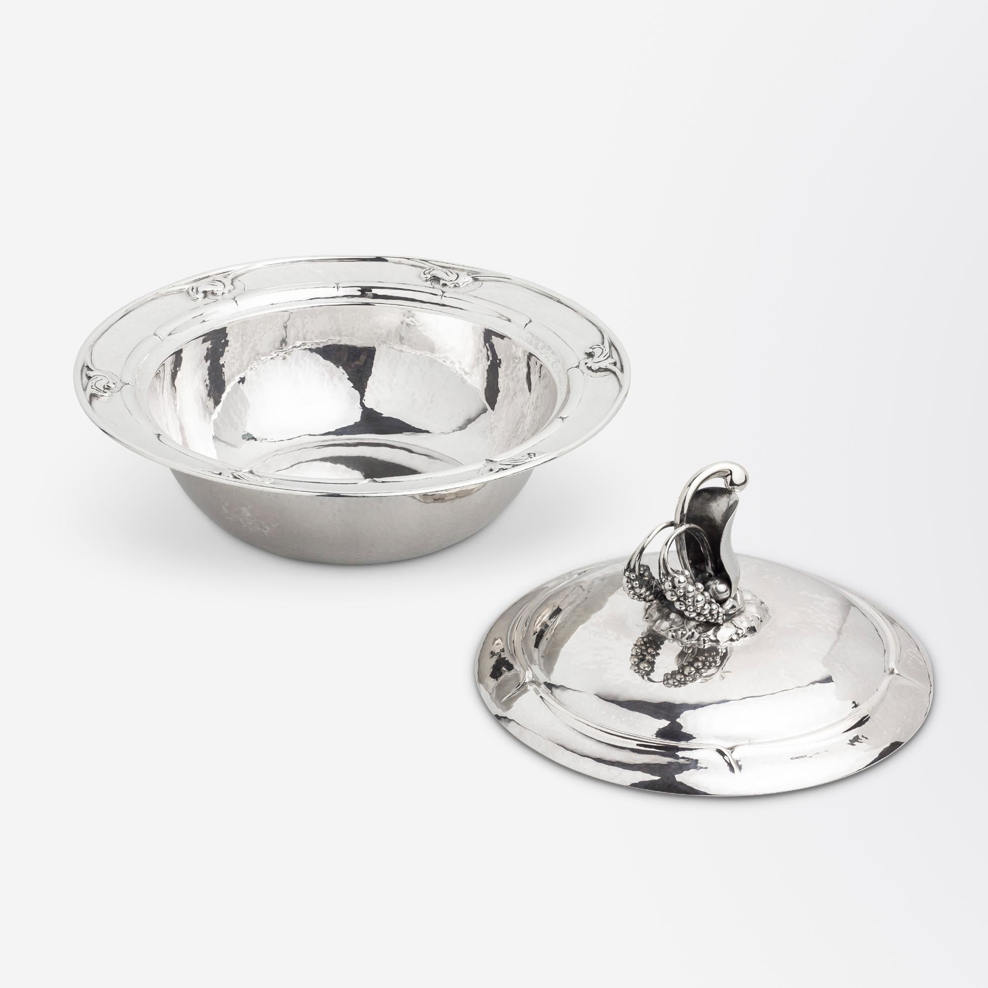 This rare piece of hand hammered sterling silver was manufactured by Danish silversmithing firm Georg Jensen during the Art Nouveau period. The piece is known as a 'lidded vegetable' dish and is completely hand hammered with an elaborate berry style