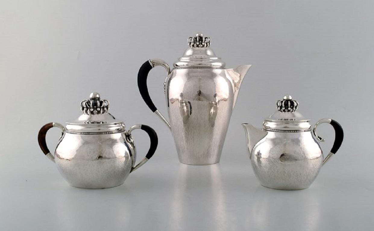 Rare Georg Jensen coffee service in sterling silver with ebony handles. 
Coffee pot, sugar bowl and cream pot. 
Lid shaped as royal crown.
Dated 1915-30.
In very good condition.
Stamped.
The coffee pot measures: 22.5 x 20 cm.
The sugar bowl
