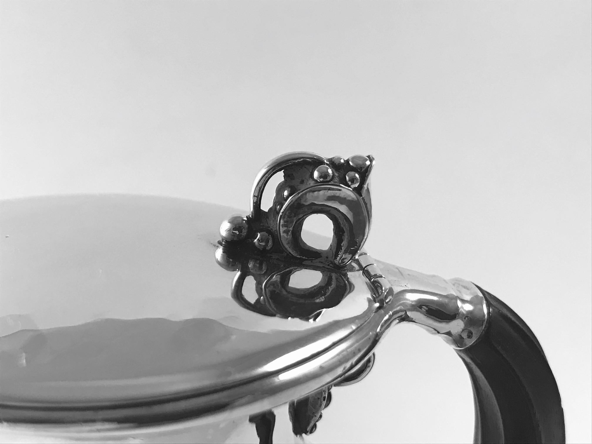 This is a rarely seen sterling silver Georg Jensen syrup jug with grape decorations on the hinged lid and under the ebony handle, design #385E by Jorgen Jensen, one of Georg Jensen’s sons.

Measures: 4 1/4? (10.5cm) in height to the top of the