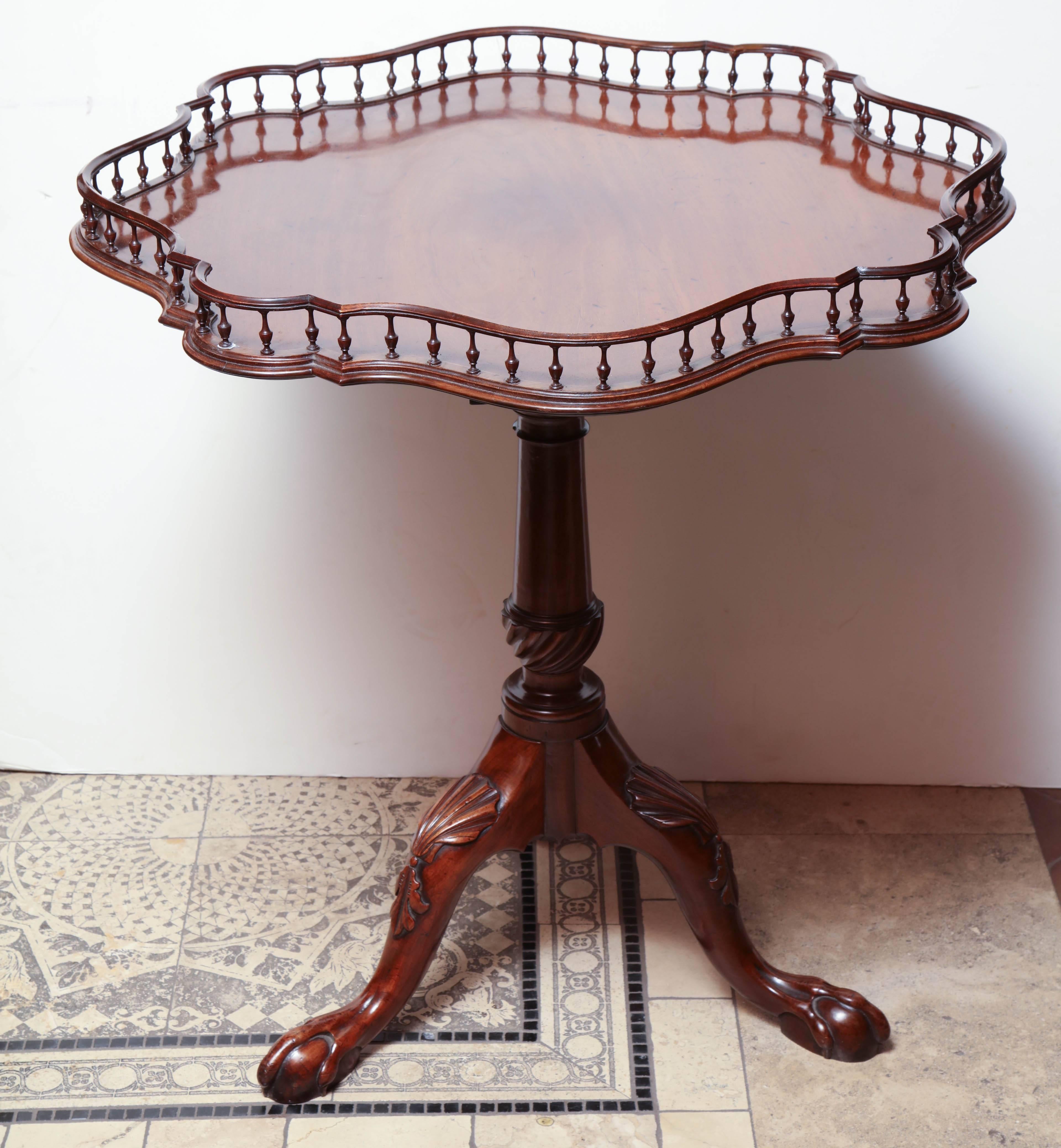 A rare English George II carved mahogany tilt-top wine table with spindle carved gallery, swirl urn form short on cabriole legs with boldly carved shell knees and ball and claw feet.