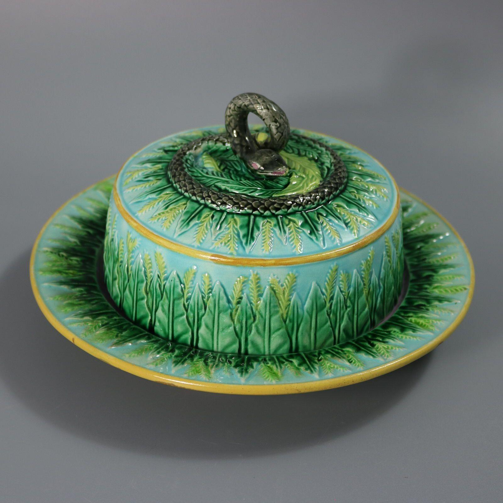 George Jones Majolica muffin dish and cover which features a snake forming the handle. Stiff leaves decorating the borders. Turquoise ground version. Colouration: green, turquoise, grey, are predominant. The piece bears maker's marks for the George
