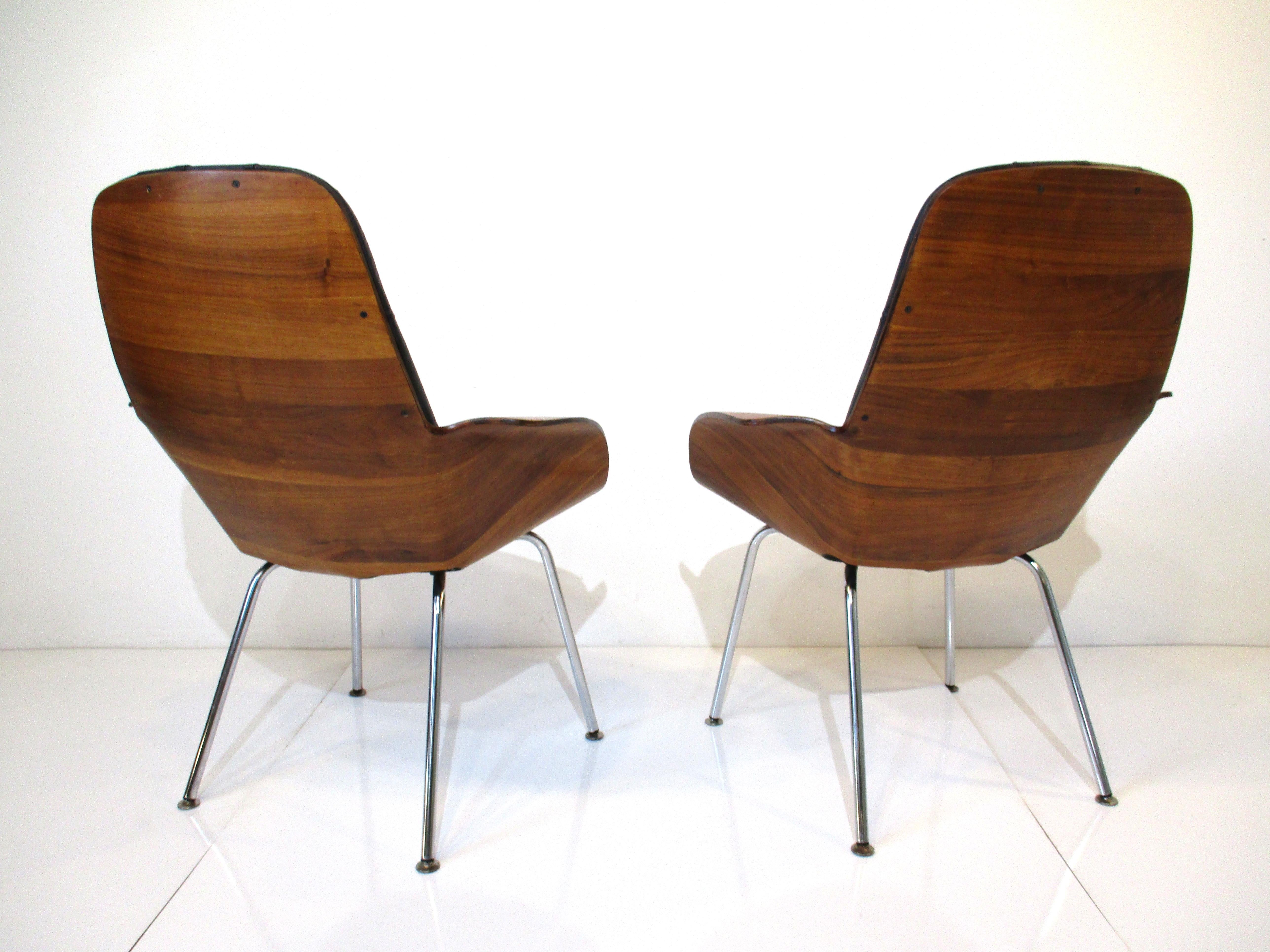 A pair of bent sculptural walnut bodied chairs with winged arms having satin black button tufted seat bottoms and backs. Sitting on chromed legs making these chairs very sturdy as they are comfortable all combined to give them a rich and