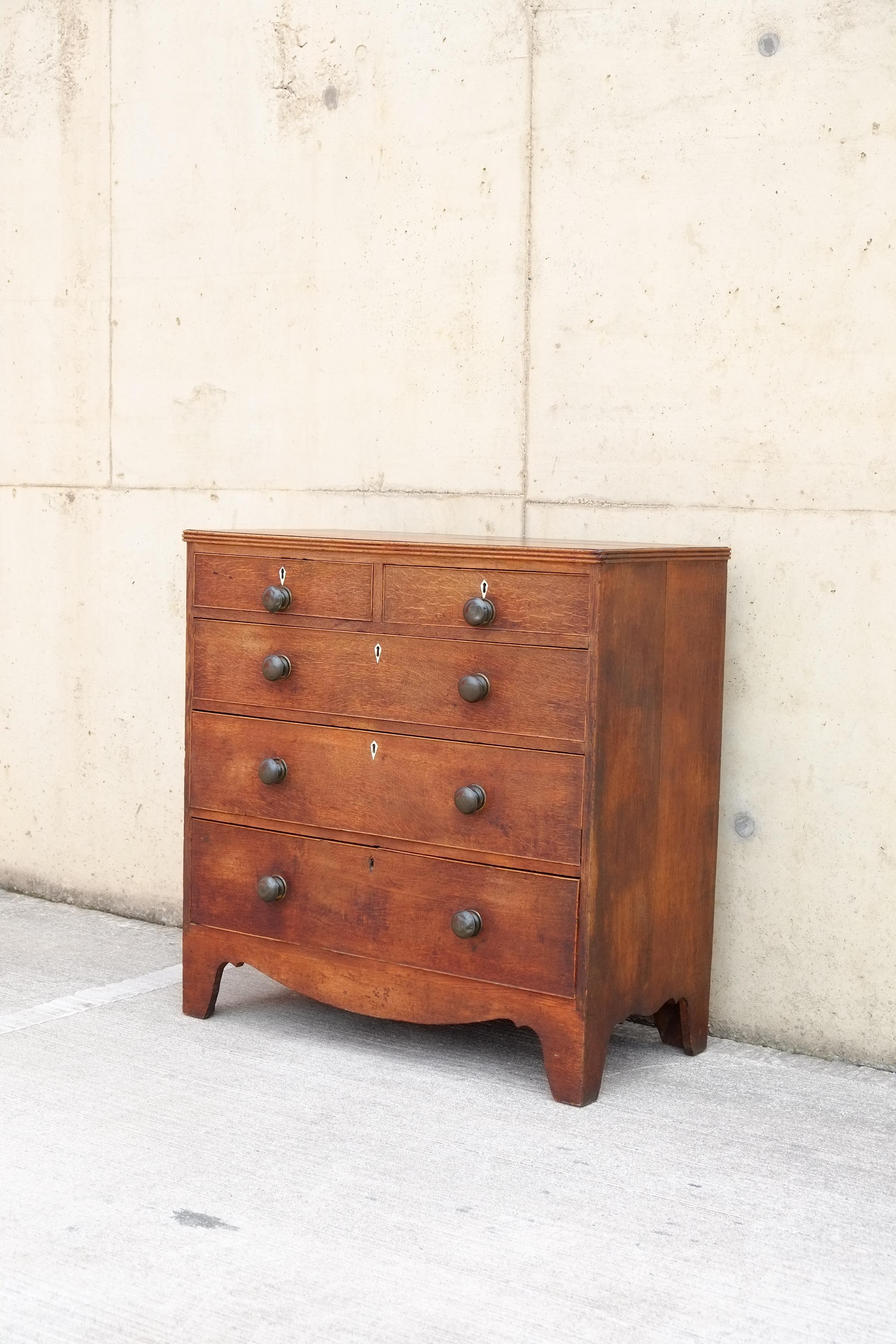 A solid oak Antique Georgian chest of drawers. This original English antique Georgian chest with five drawers has gorgeous colour and patina in solid oak. Beautiful blackened brass knobs with lots of character, they have inlaid cream diamonds above