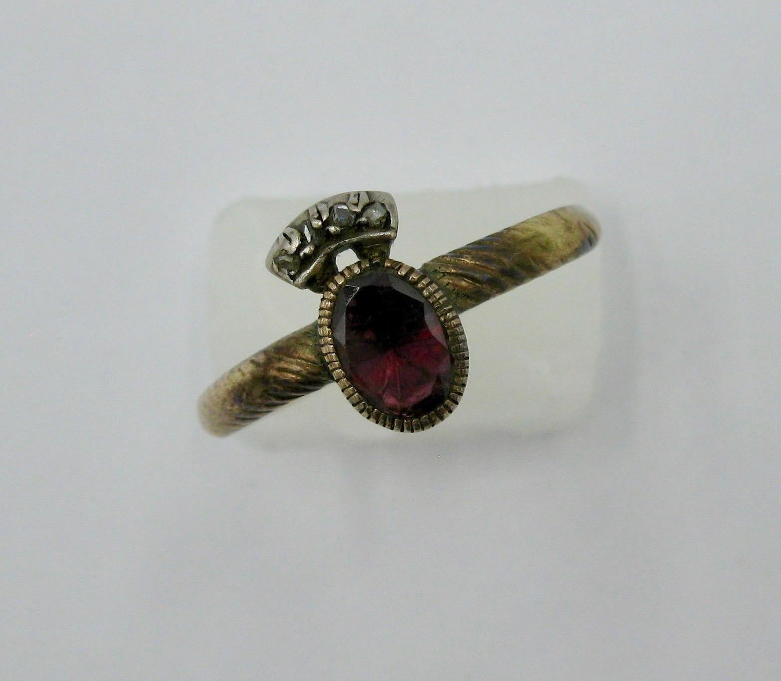 A very early Georgian ring with an oval flat cut Almandine Garnet crowned with four Rose Cut Diamonds and dating to the 1700s.  A museum quality jewel from the collection of Edith Weber.  The gold is 12 Karat Gold and the diamonds are set in silver