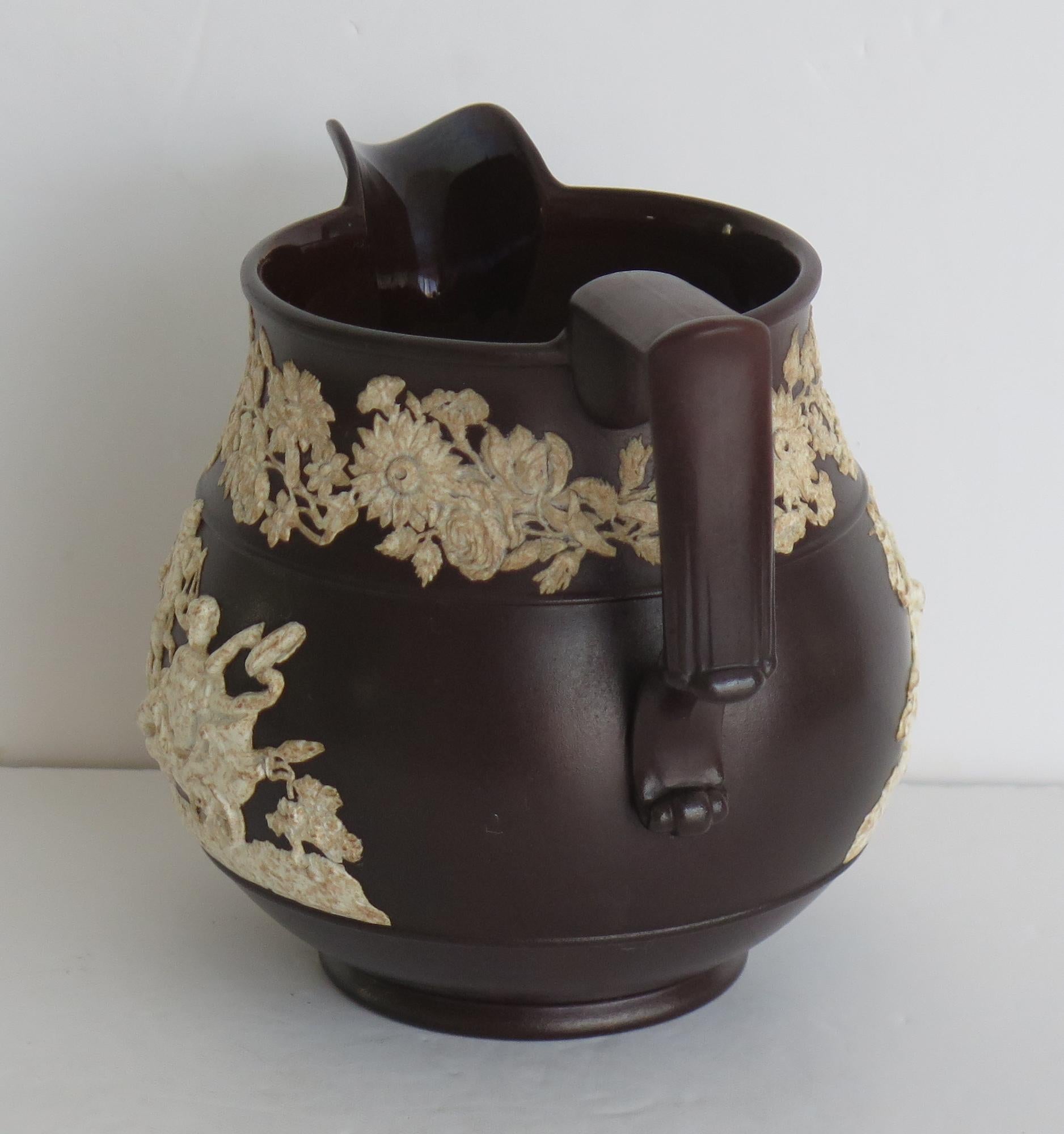This is a rare antique earthenware pottery jasperware jug or pitcher by David Wilson and Sons of Hanley, formerly Robert Wilson, dating to the very early 19th Century, late Georgian period, circa 1810. 

The jug has a dark brown glaze with applied