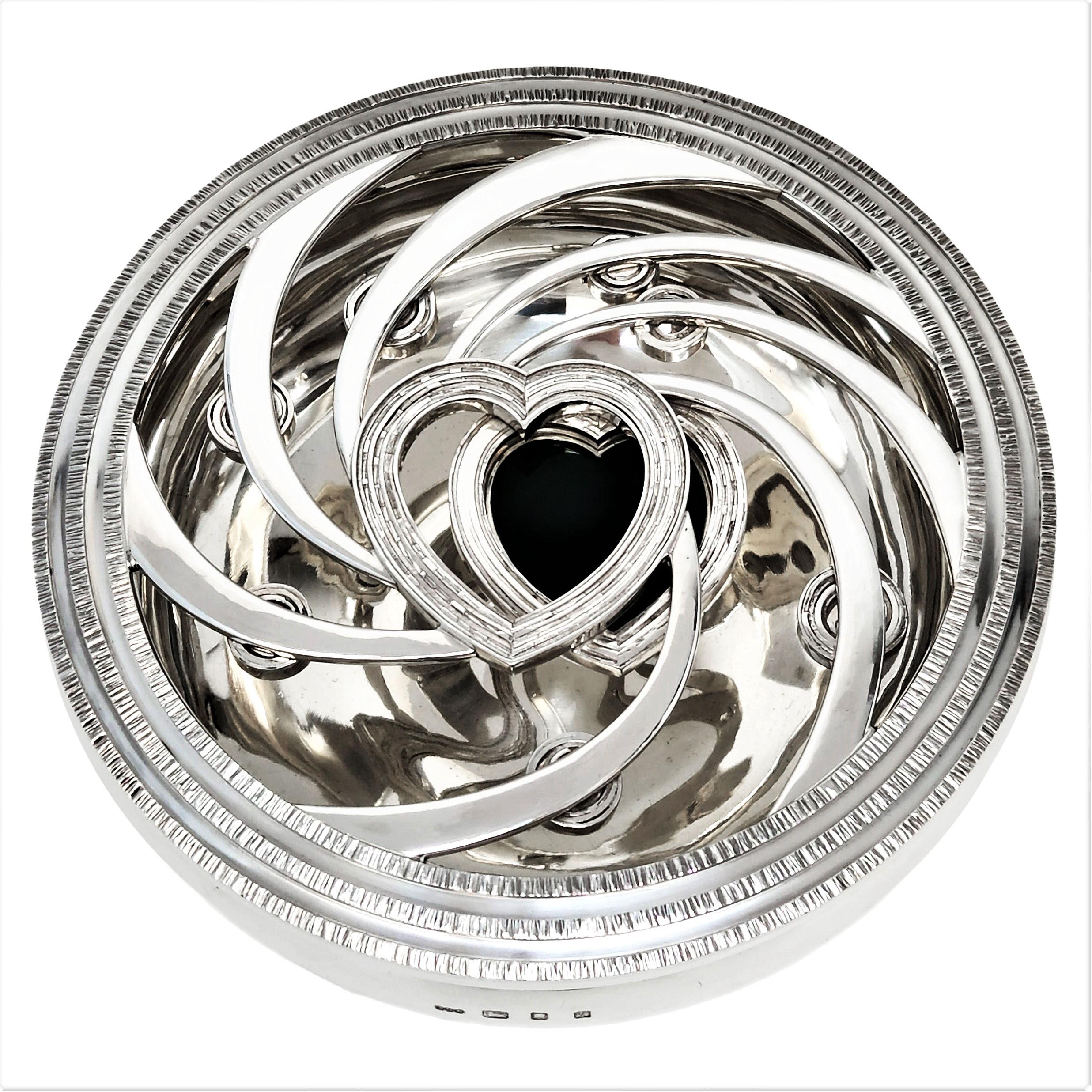 A magnificent Elizabeth II sterling silver covered bowl by Gerald Benney. This Centrepiece features an elegant lightly hammered bowl with a deep open work cover cast with swirl designs culminating in two hearts, one open and the other with a deep