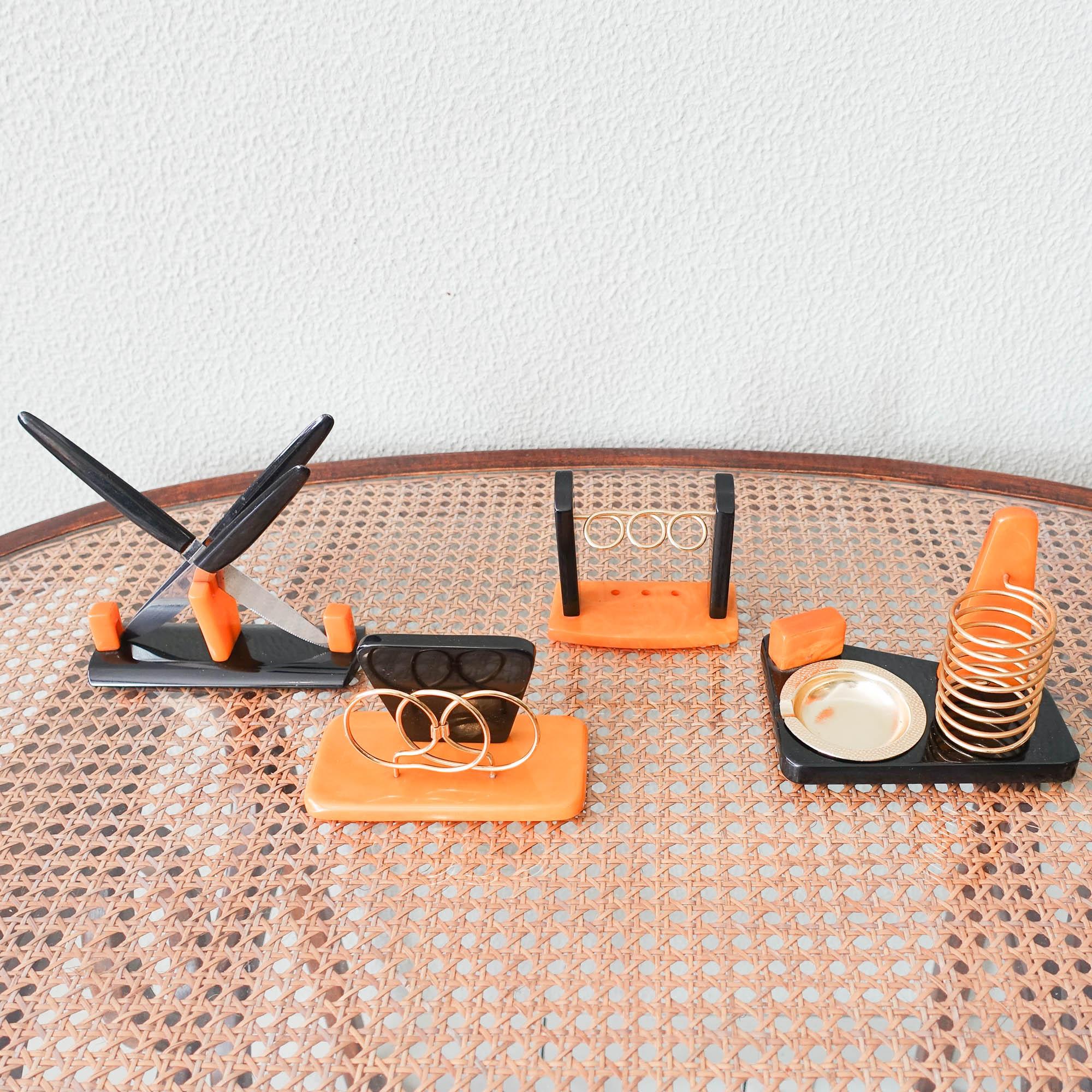 This rare desk set was designed and produced in Germany, during the 1940's. It consists on a knives holder, with three knives, a letter holder, an ashtray and cigarettes holder and a pen holder. All pieces are in bakelite amber honey shade and black