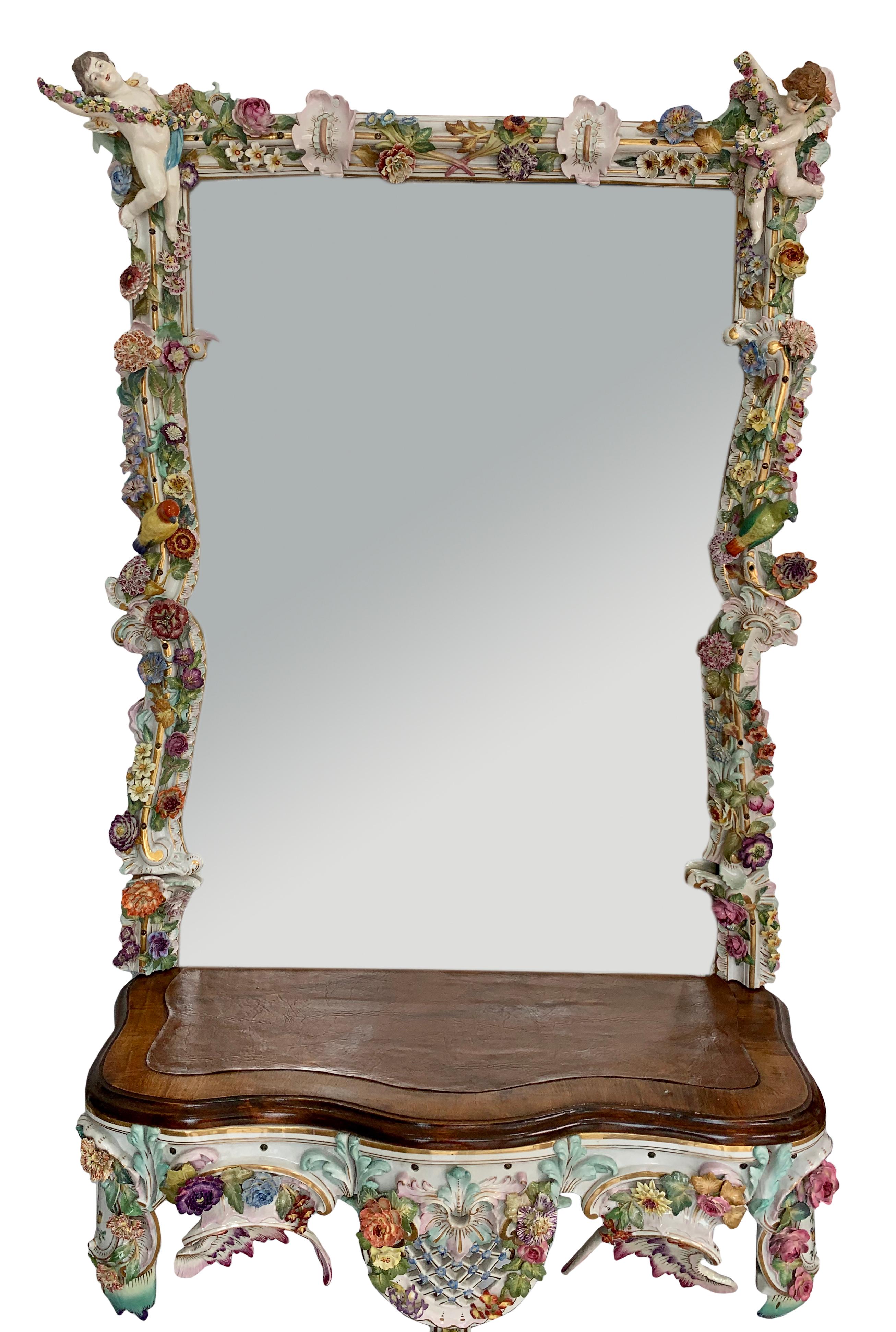 A very rare early 20th century German Rococo style hand painted porcelain figural console and mirror. The rectangular plate within a border richly decorated with flowers, birds, foliage, flanked by two cherubs holding garlands of flowers resting on
