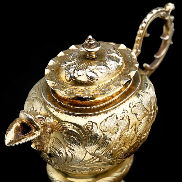 A rare German silver gilt ewer; mark of Martin II Heuglin, Augsburg 1659–1663. The bowl with scroll handle and grotesque mask spout, on a spreading food and with detachable cover. The foot, body and cover each chased with foliage and flowers, the