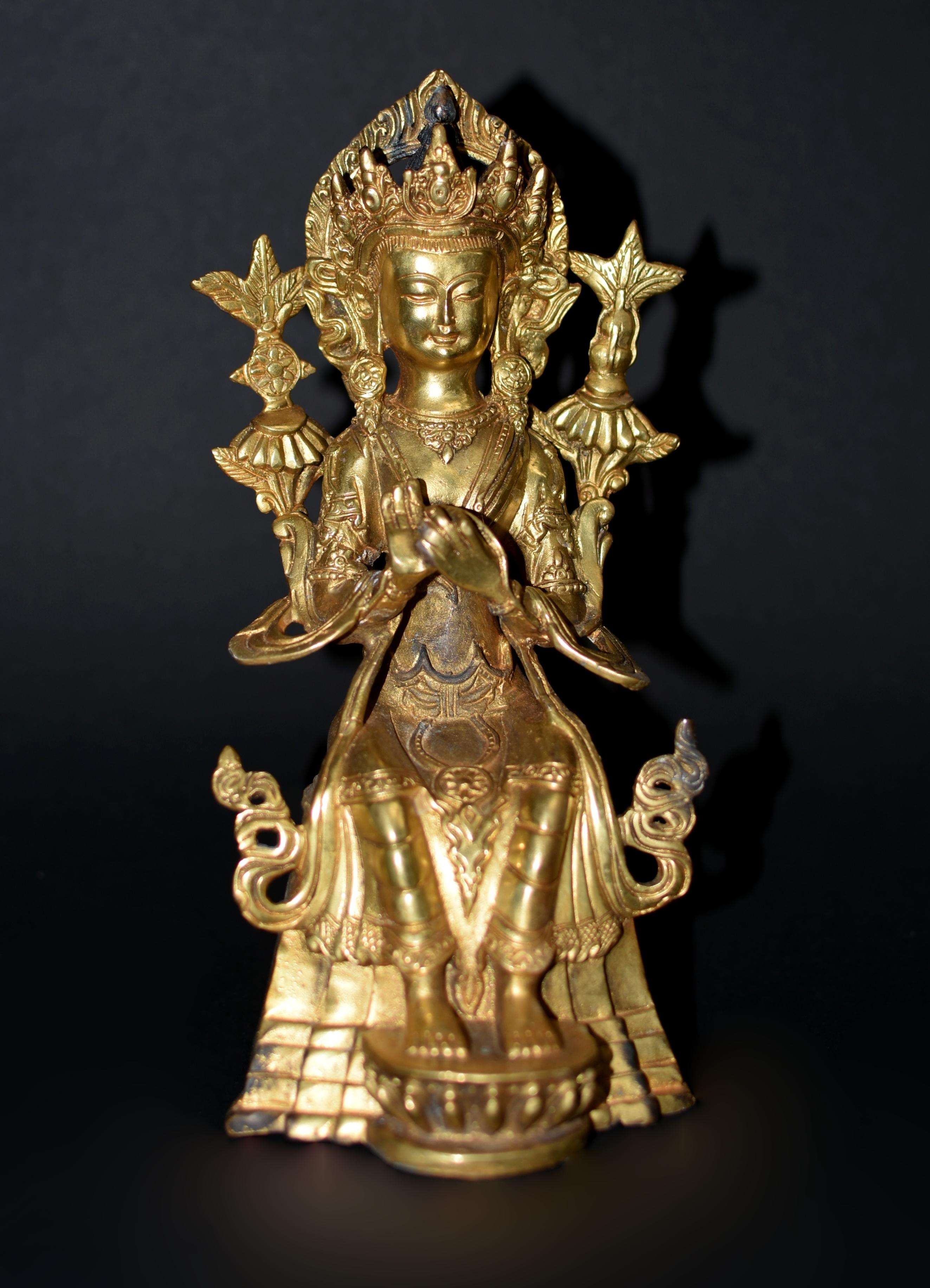Eine besondere Statue des tibetischen Bodhisattva Maitreya, des zukünftigen Buddhas. Dargestellt auf einem hohen Lotusthron sitzend, mit einer großen verzierten Krone vor einer flammenförmigen Mandola und einem Paar Blumenpfosten, langen Ohrringen,
