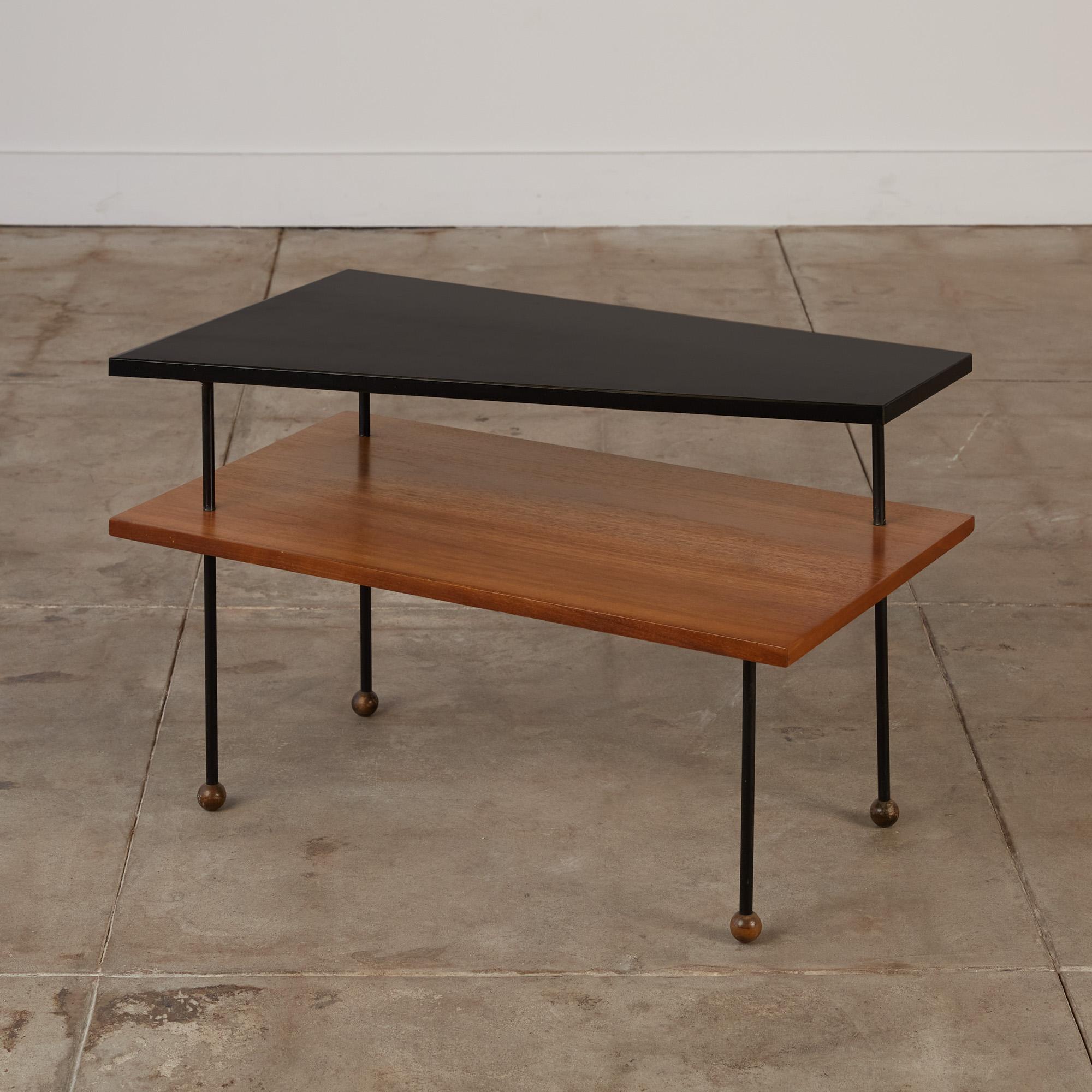 Rare Greta Grossman side table for Glenn of California, circa 1950s. The table features an asymmetrical black laminate shelf that sits atop a rectangular walnut shelf. The shelves are held together by four thin painted metal stems with wooden ball