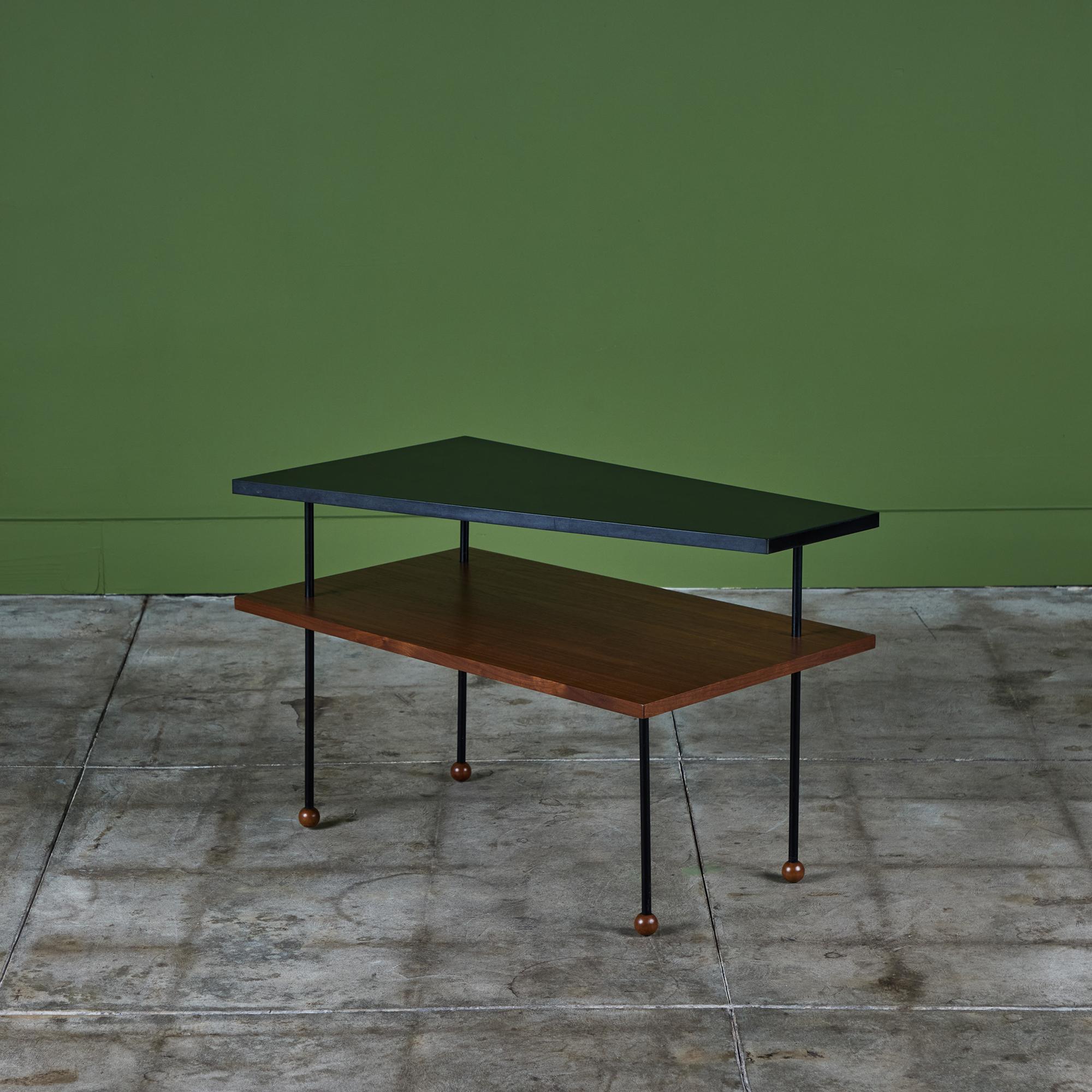 Rare Greta Grossman side table for Glenn of California, c.1950s. The table features an asymmetrical black laminate shelf that sits atop a rectangular walnut shelf. The shelves are held together by four thin painted metal stems with wooden ball feet.
