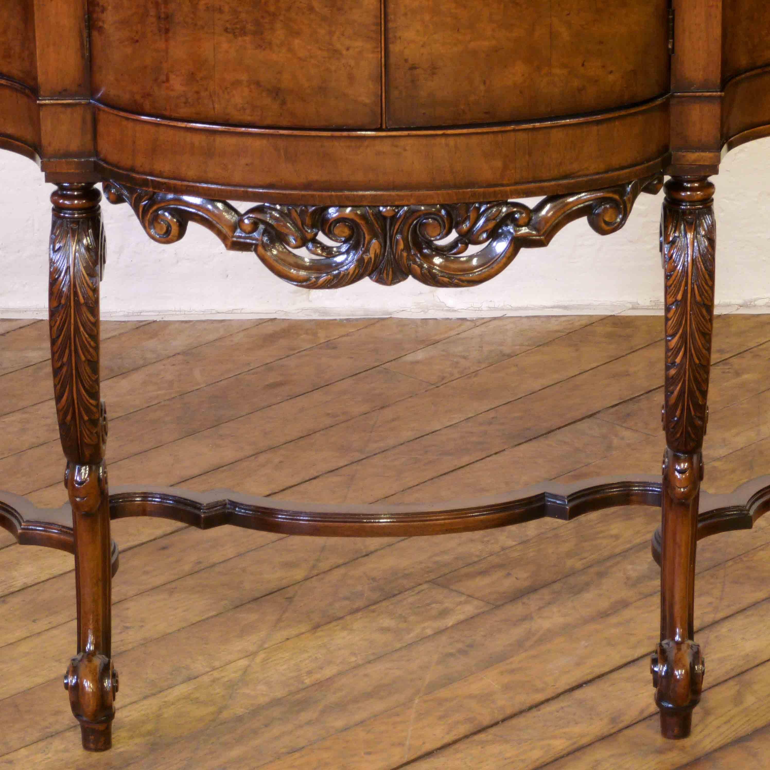 This is an unusually small burr walnut sideboard/credenza manufactured shortly after the First World War. The baroque styled undercarriage is of 4 cabriole shaped legs, with carved acanthus to the shoulder and terminating on a scrolled feet. All