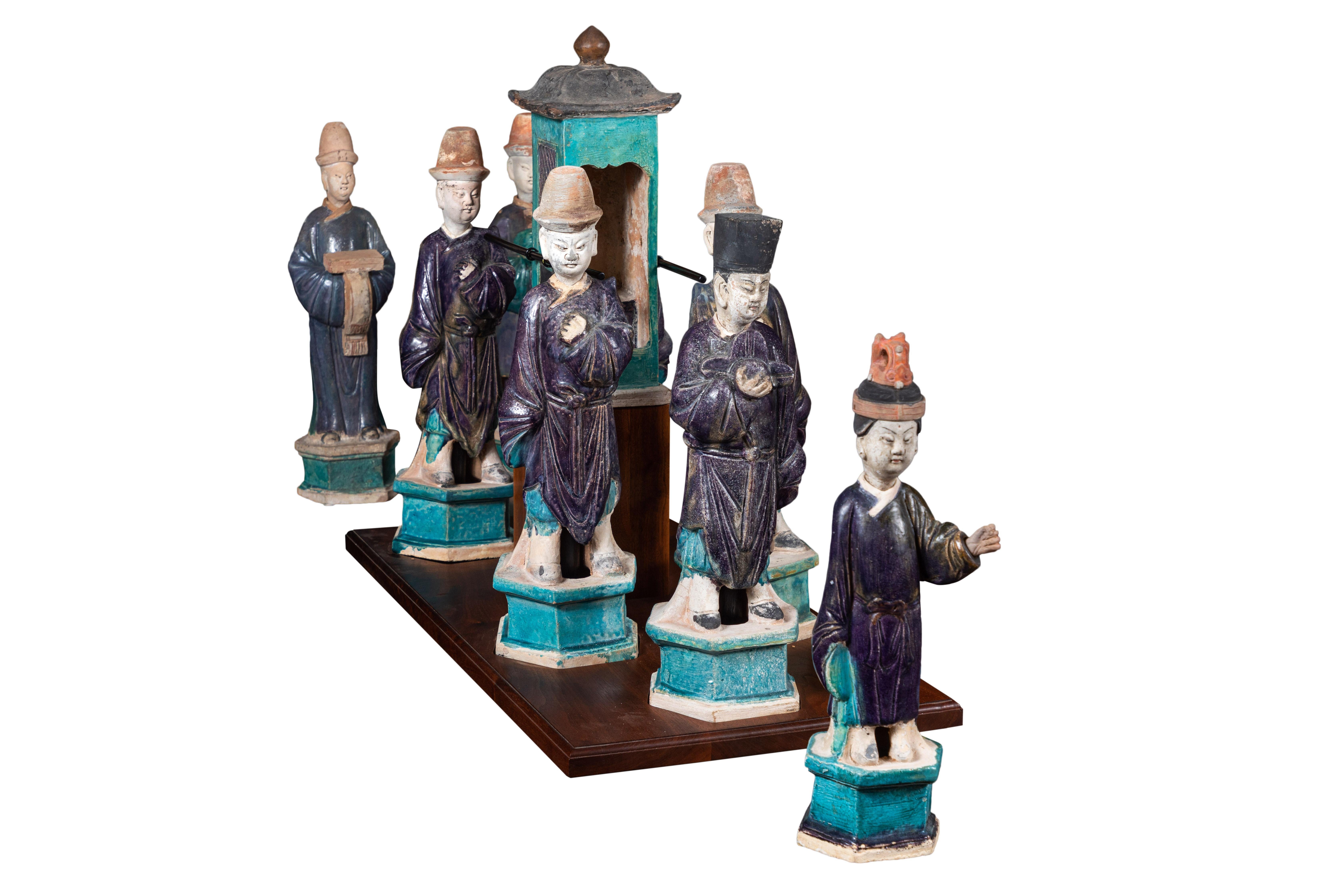 Beautiful and unusual, hand-molded, painted and glazed, eight-person procession of robed attendants both surrounding, and bearing a litter born on poles. The central figures and litter are now mounted on a custom, wood base. 

Note: Measurements