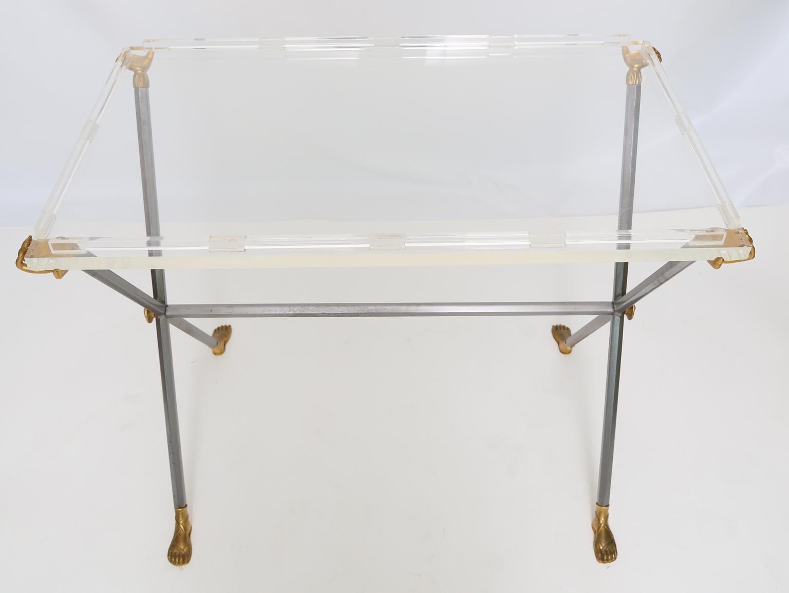 Unusual tray table, having a rectangular top of Lucite, on X-frame stand of steel and brass, joined by stretcher, four-cast hands hold the acrylic table surface, with four sandaled feet finishing the base. 

Stock ID: D2532.